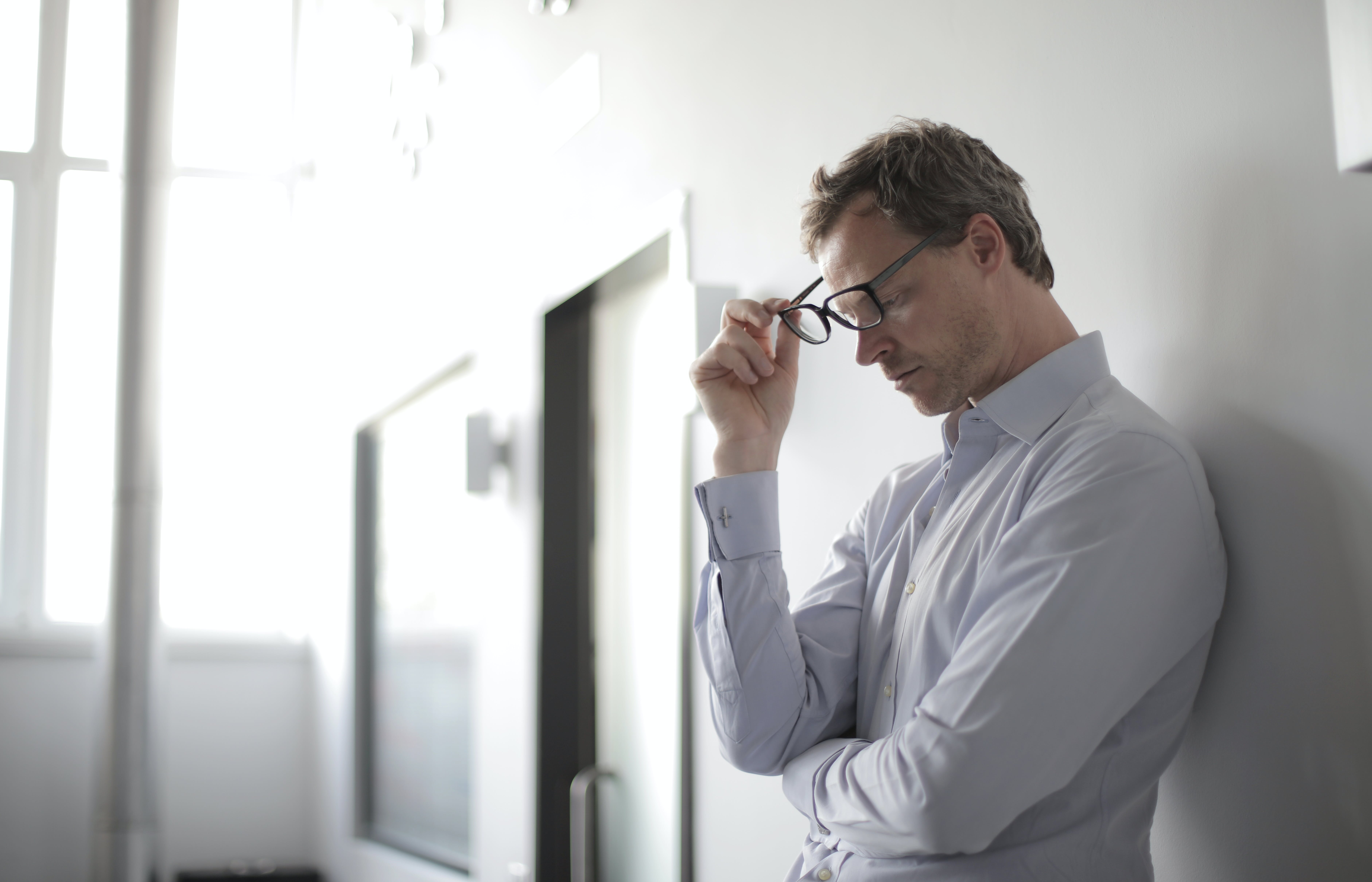 Un homme contrarié tenant ses lunettes contre son visage tout en se tenant contre un mur | Source : Pexels