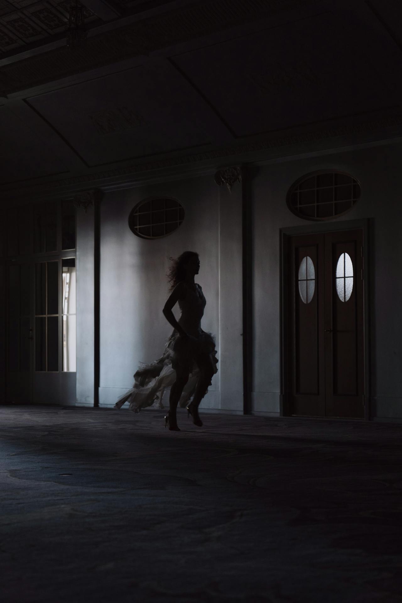 Silhouette d'une femme courant dans un couloir faiblement éclairé | Source : Pexels