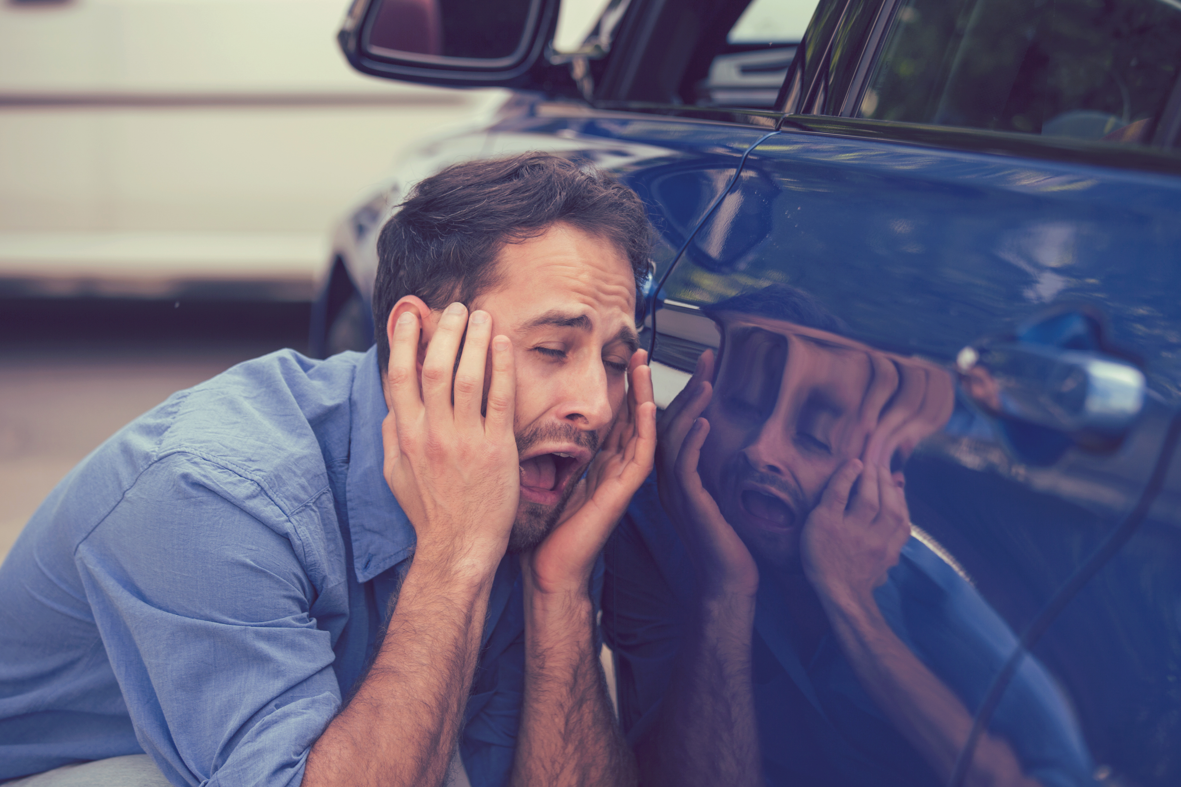 Jeune homme contrarié et frustré regardant les rayures et les bosses sur sa voiture | Source : Getty Images