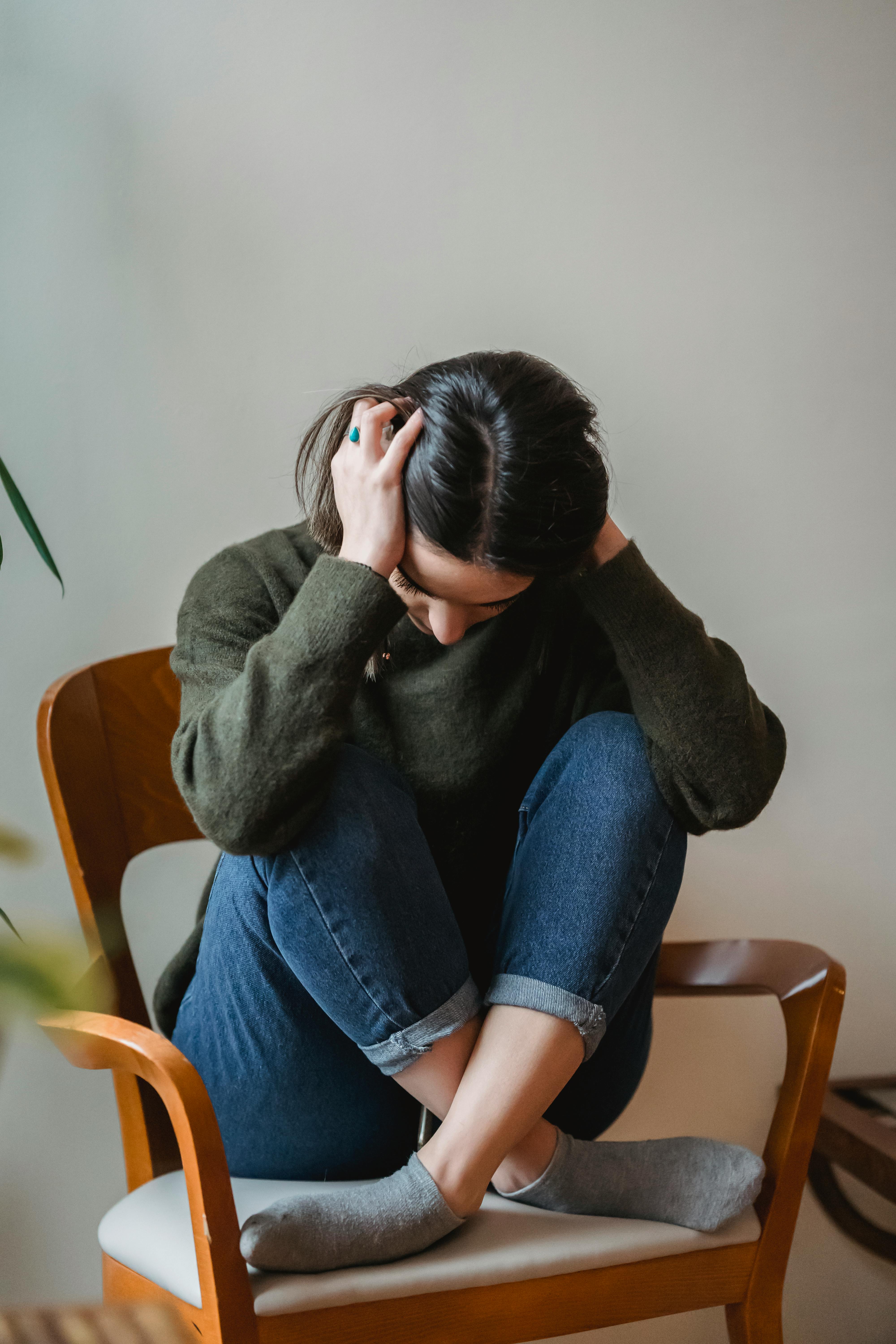 Une femme assise sur une chaise, se tenant la tête en signe de désespoir | Source : Pexels