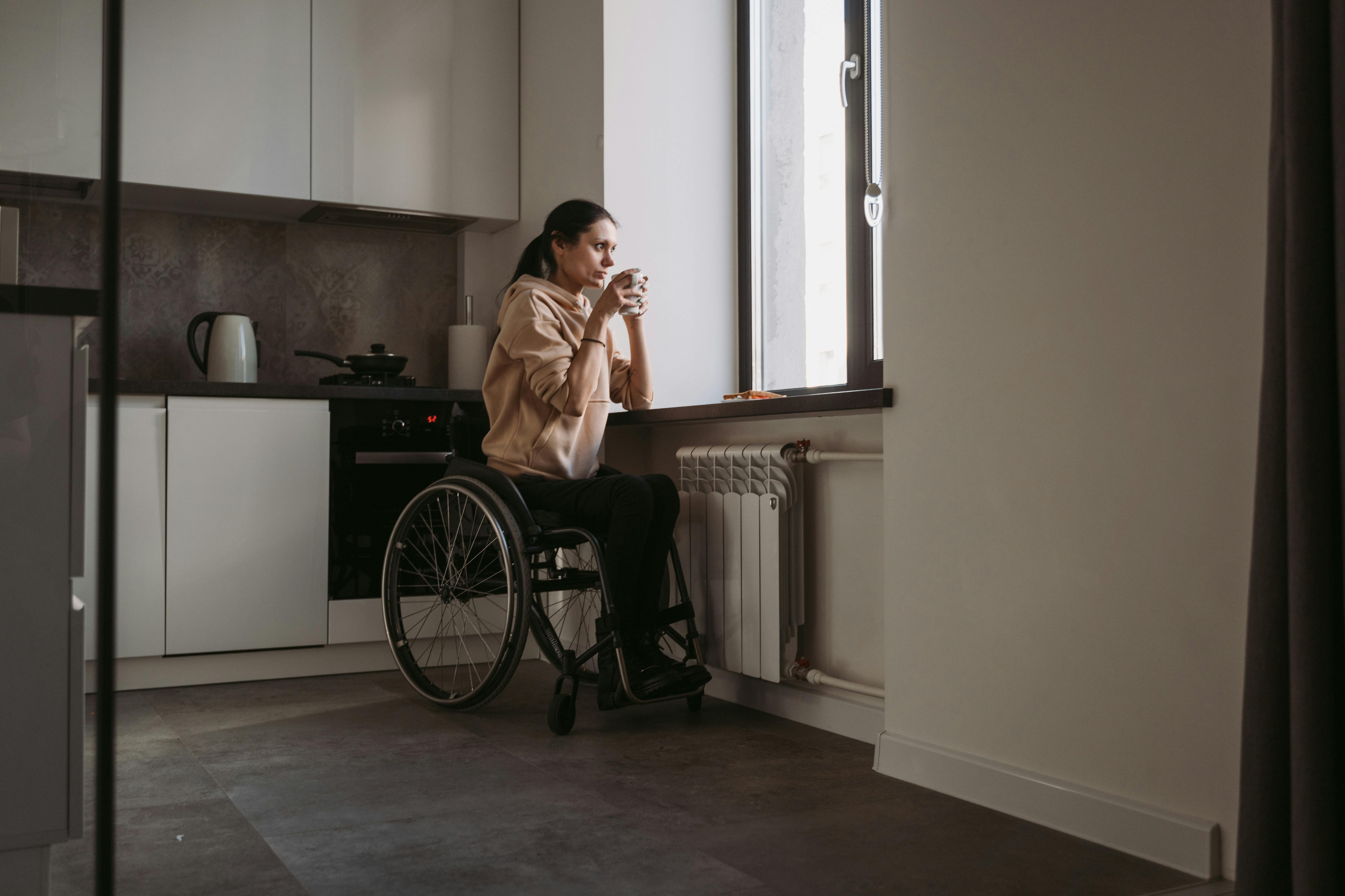 Une jeune femme en fauteuil roulant boit un café en regardant par la fenêtre en pensée. À des fins d'illustration uniquement | Source : Pexels