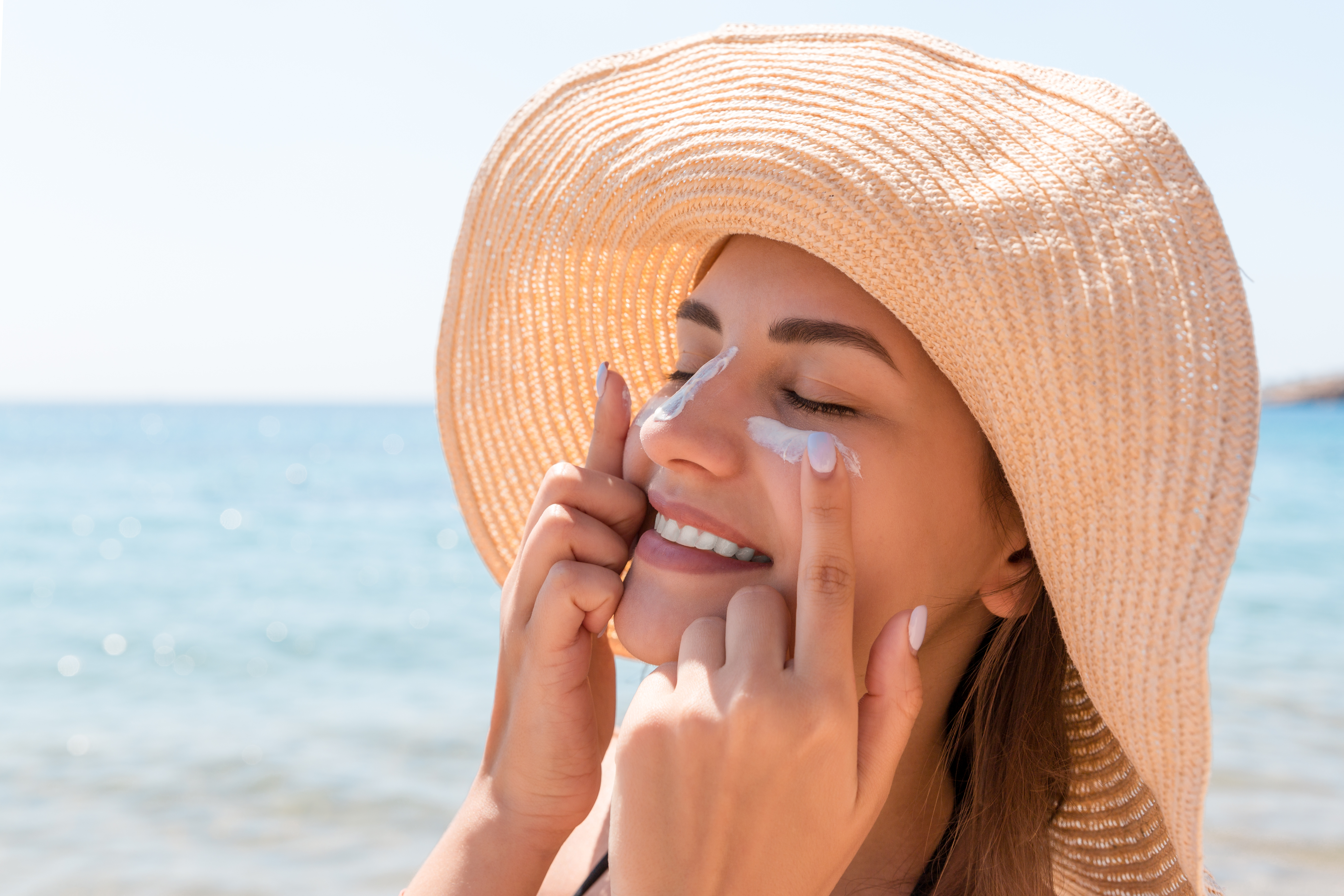 Femme appliquant de la crème solaire sur son visage à la plage | Source : Shutterstock