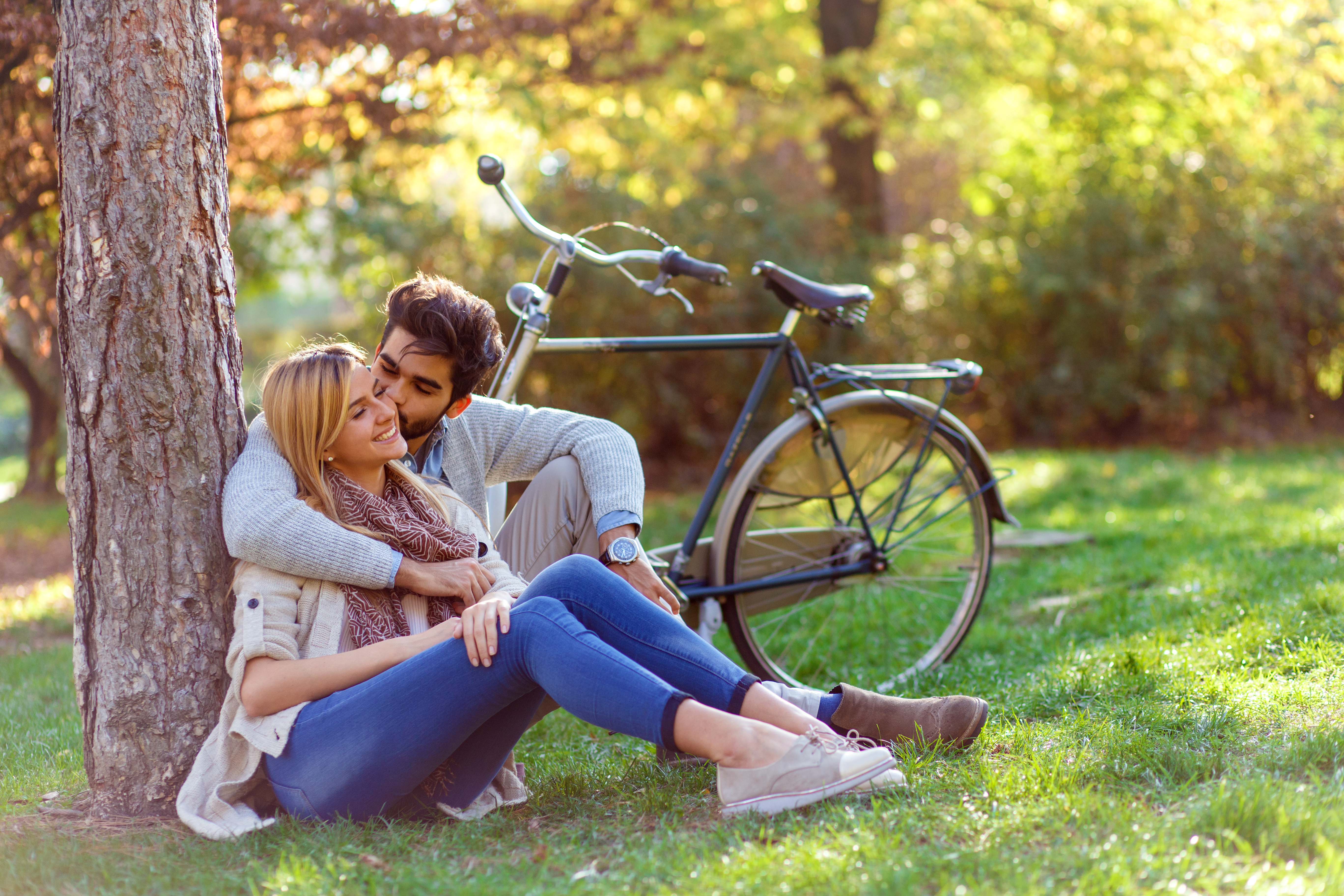 Un jeune couple amoureux photographié assis dans un parc en train de s'adosser à un arbre et de s'embrasser | Source : Shutterstock