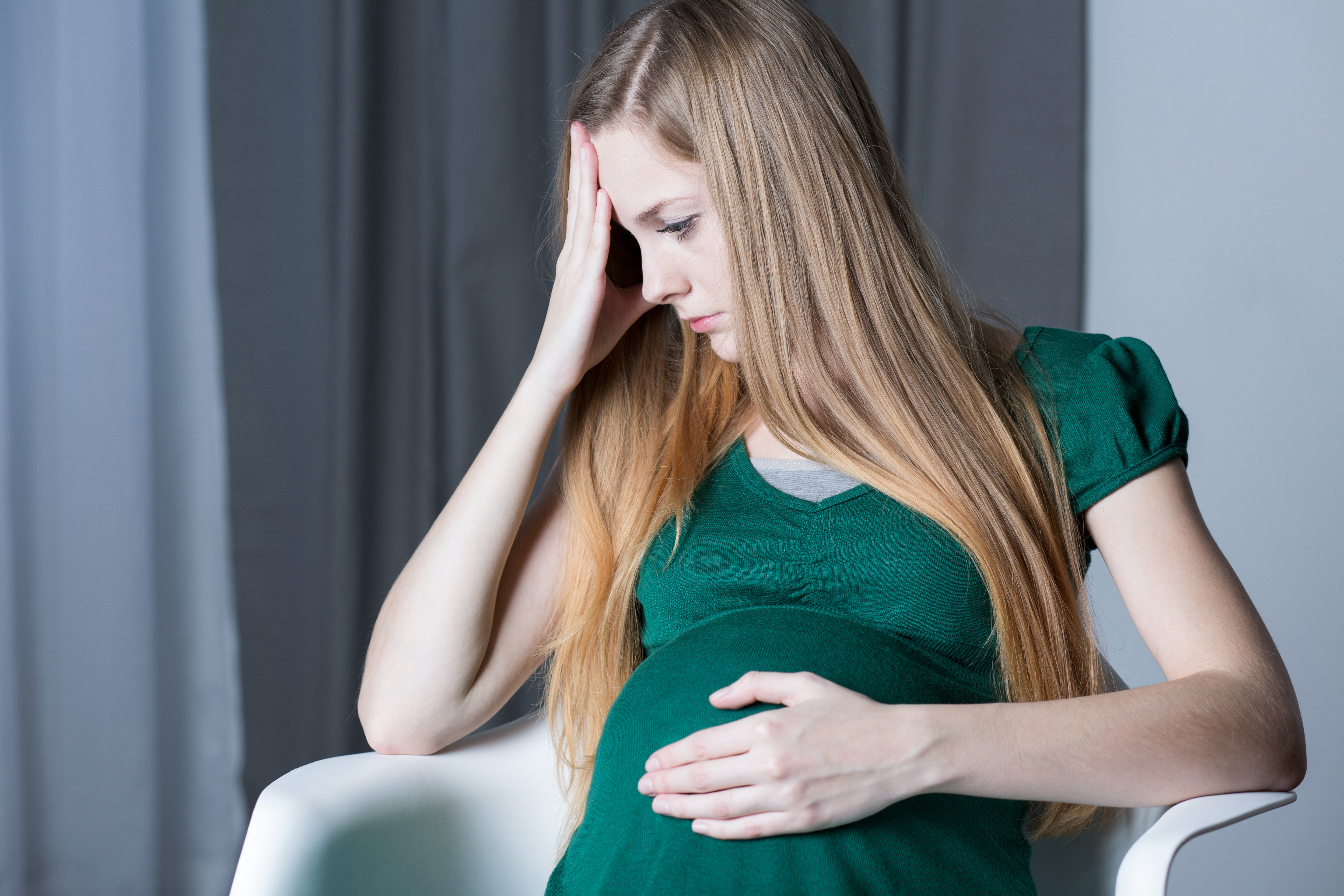 Une femme enceinte bouleversée, assise et se tenant la tête et le ventre | Source : Shutterstock