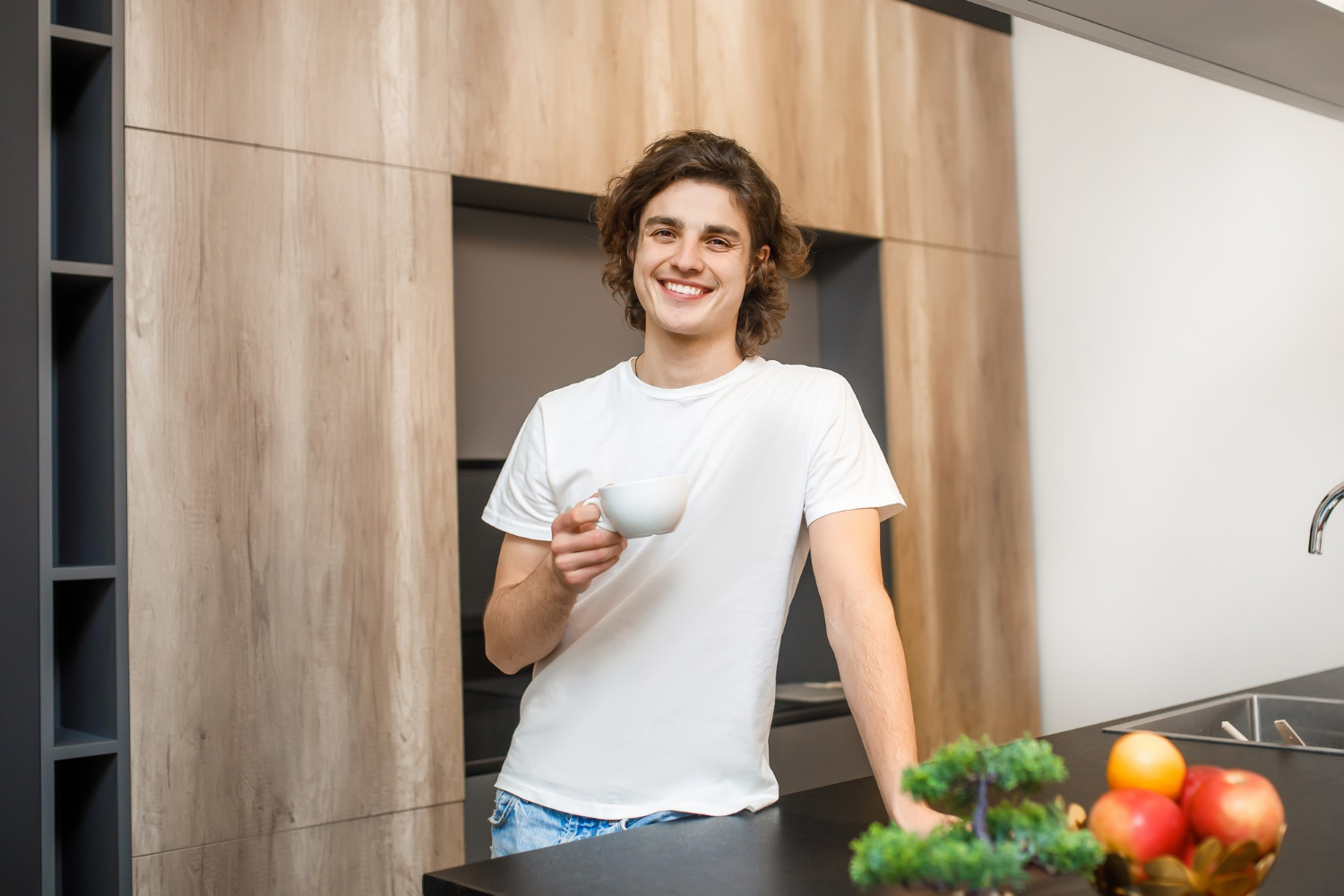 Un homme souriant tenant une tasse en céramique blanche et se tenant dans la cuisine | Source : Freepik