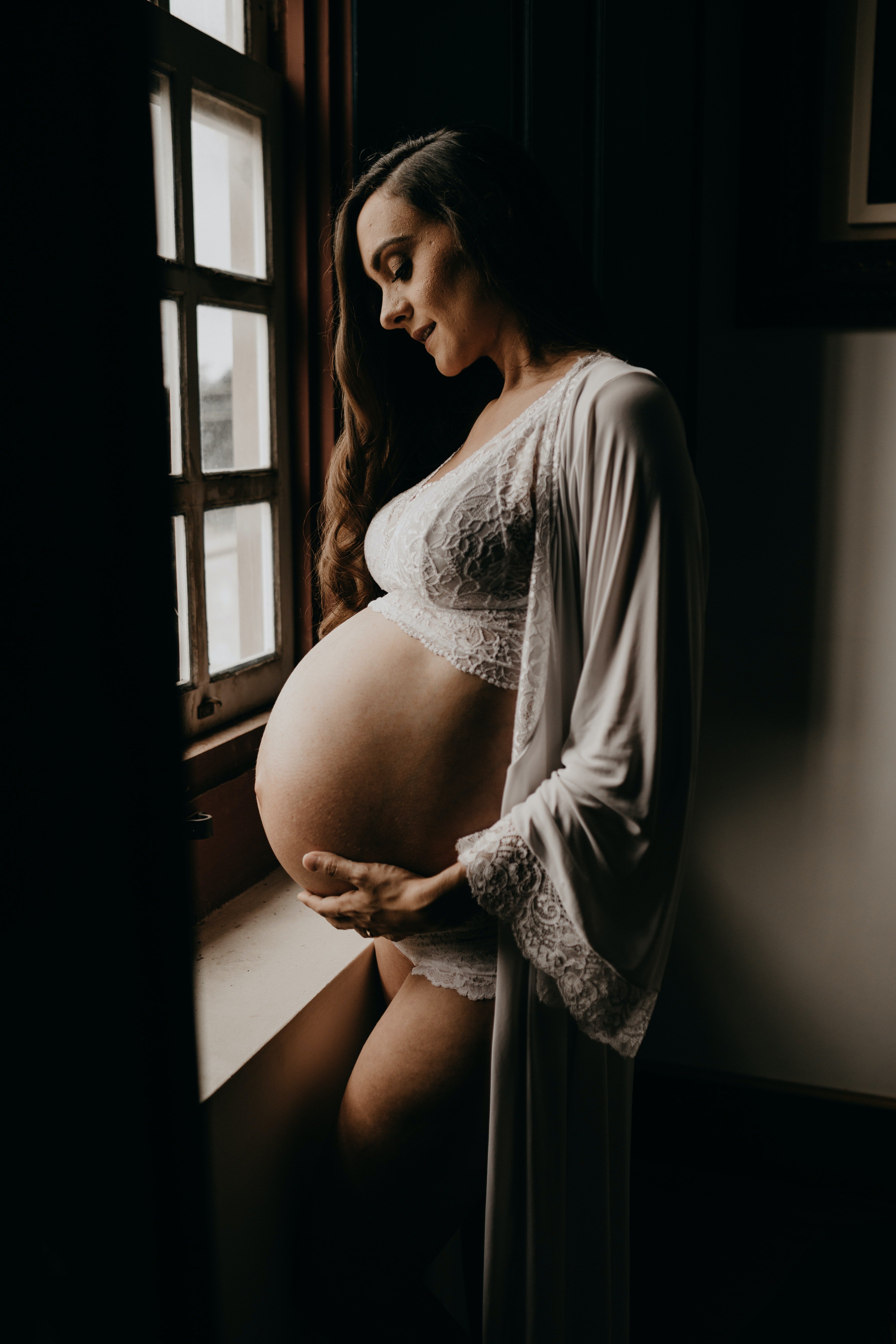 Femme enceinte portant un gilet à côté d'une fenêtre. | Source : Pexels