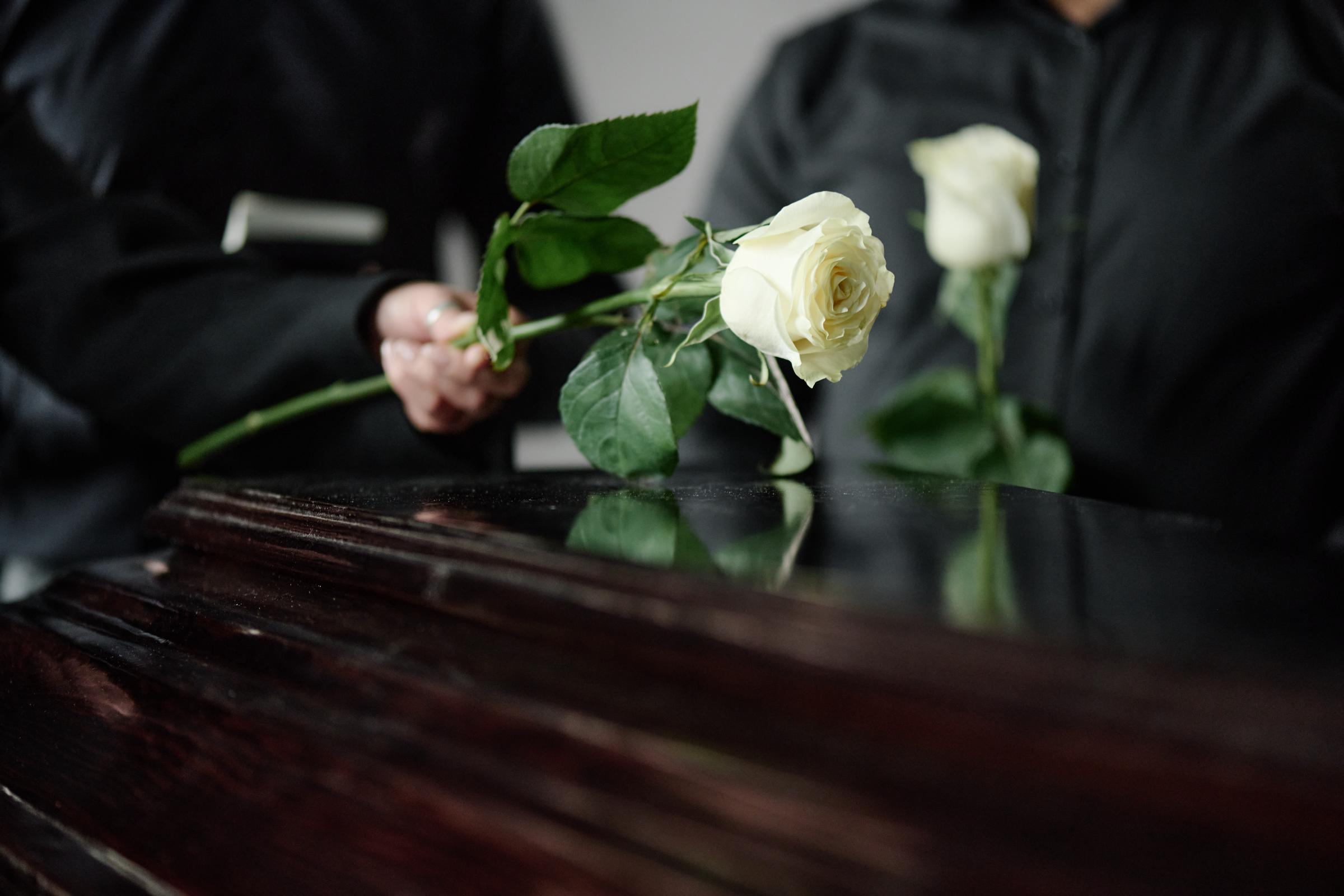 Une personne tenant une fleur près d'un cercueil | Source : Shutterstock