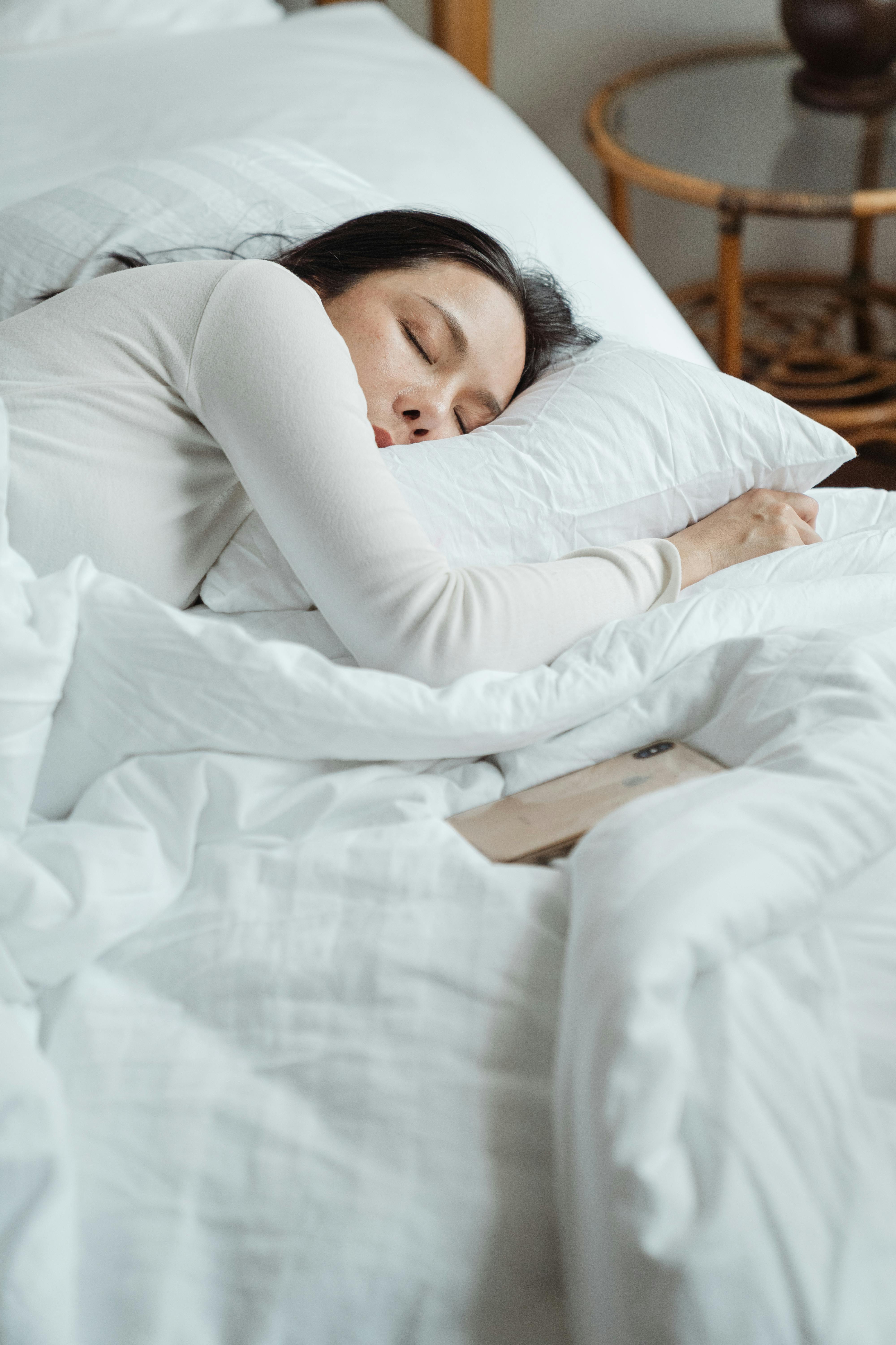 Une femme allongée dans son lit, seule, avec son téléphone sur le côté | Source : Pexels