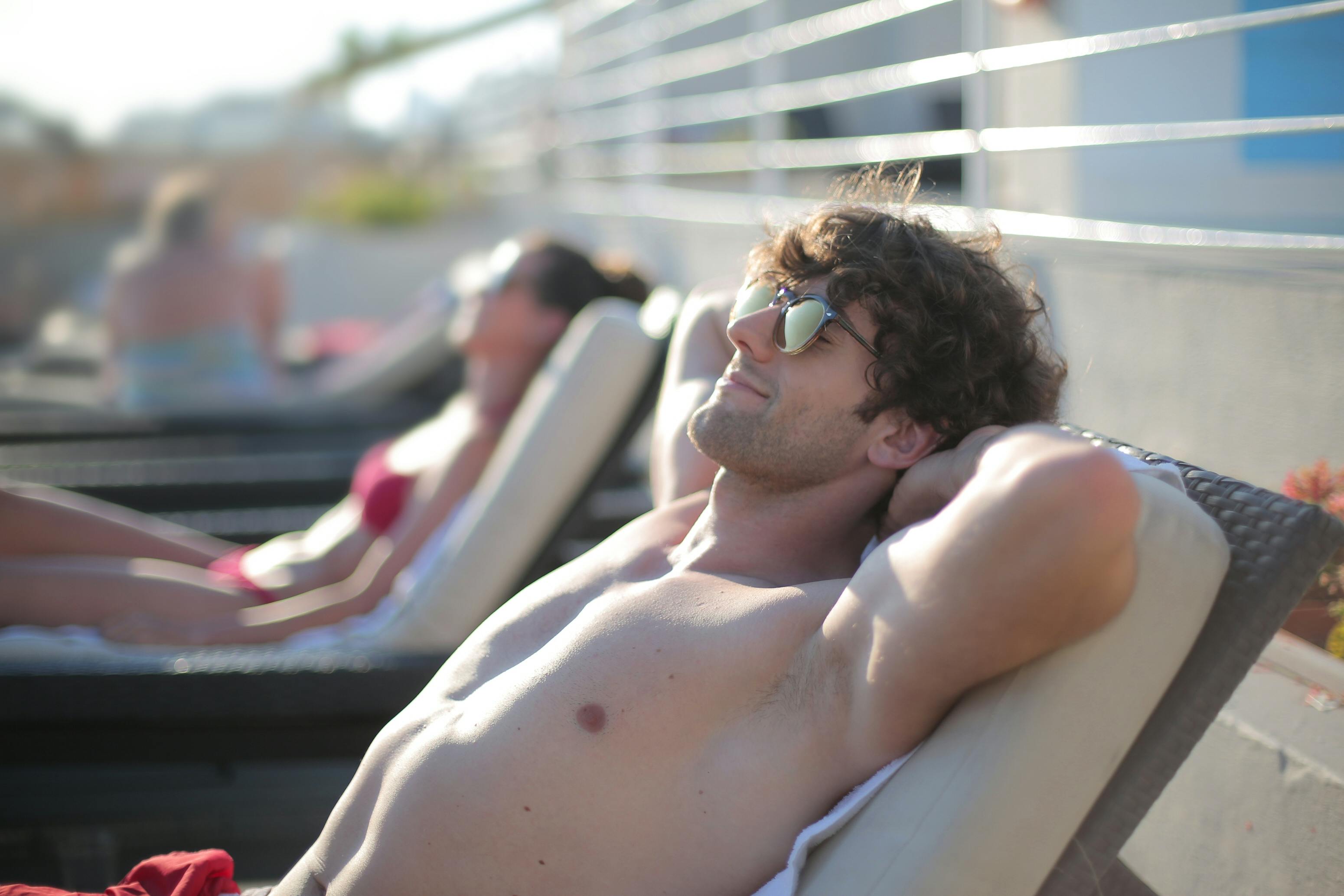 Un homme heureux portant des lunettes de soleil alors qu'il est allongé sur un transat | Source : Pexels