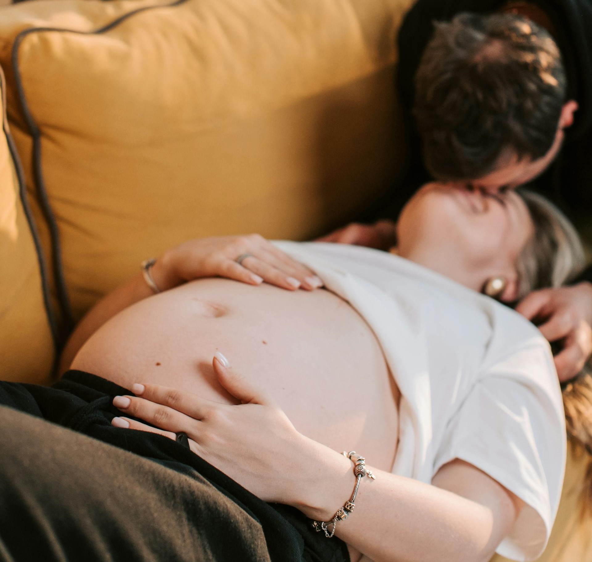 A pregnant woman lying down while her partner kisses her | Source: Pexels