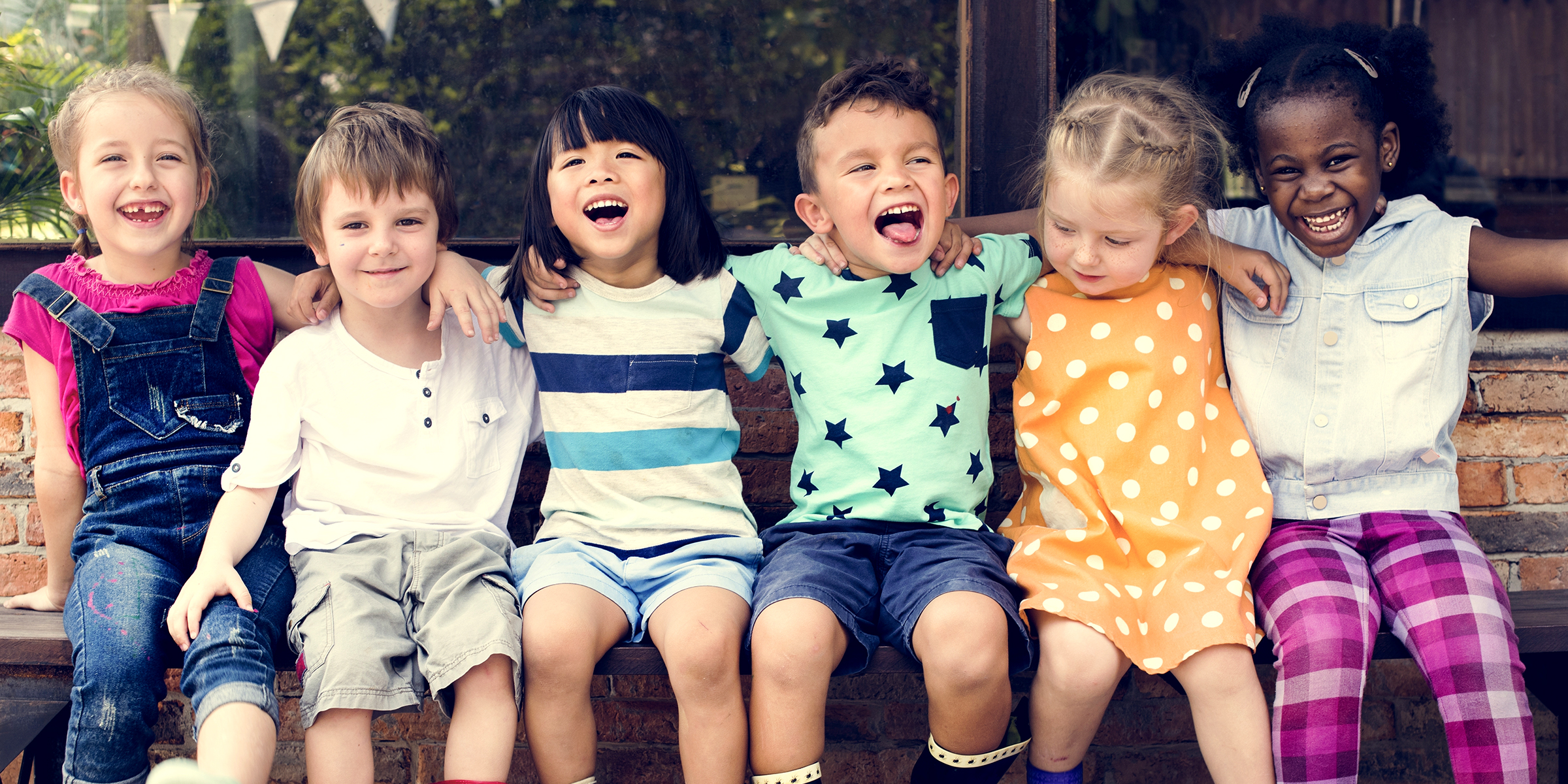 Des petits enfants joyeux assis sur un banc et riant | Source : Shutterstock