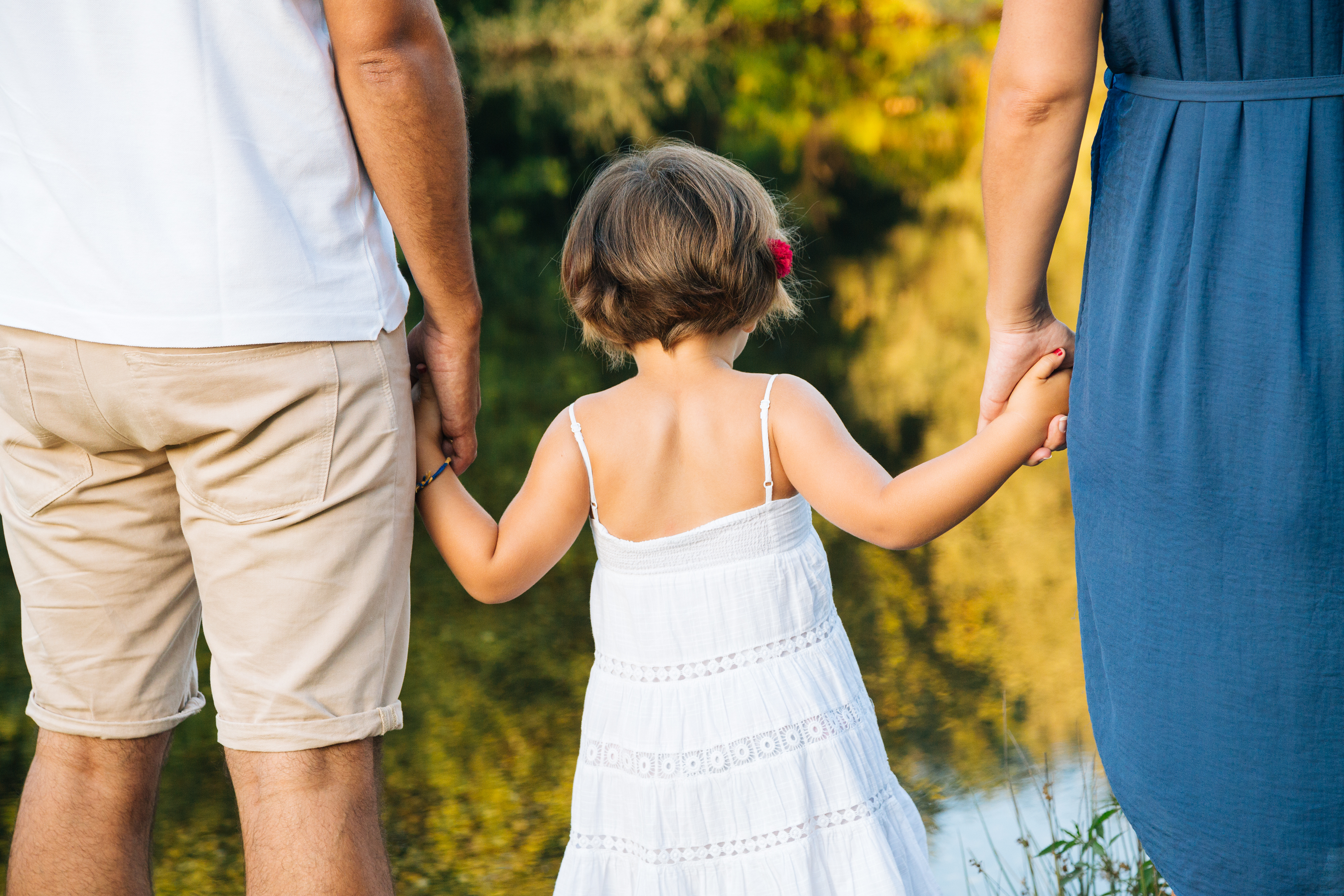 Une petite fille tient la main de ses parents tout en marchant sur le rivage | Source : Shutterstock