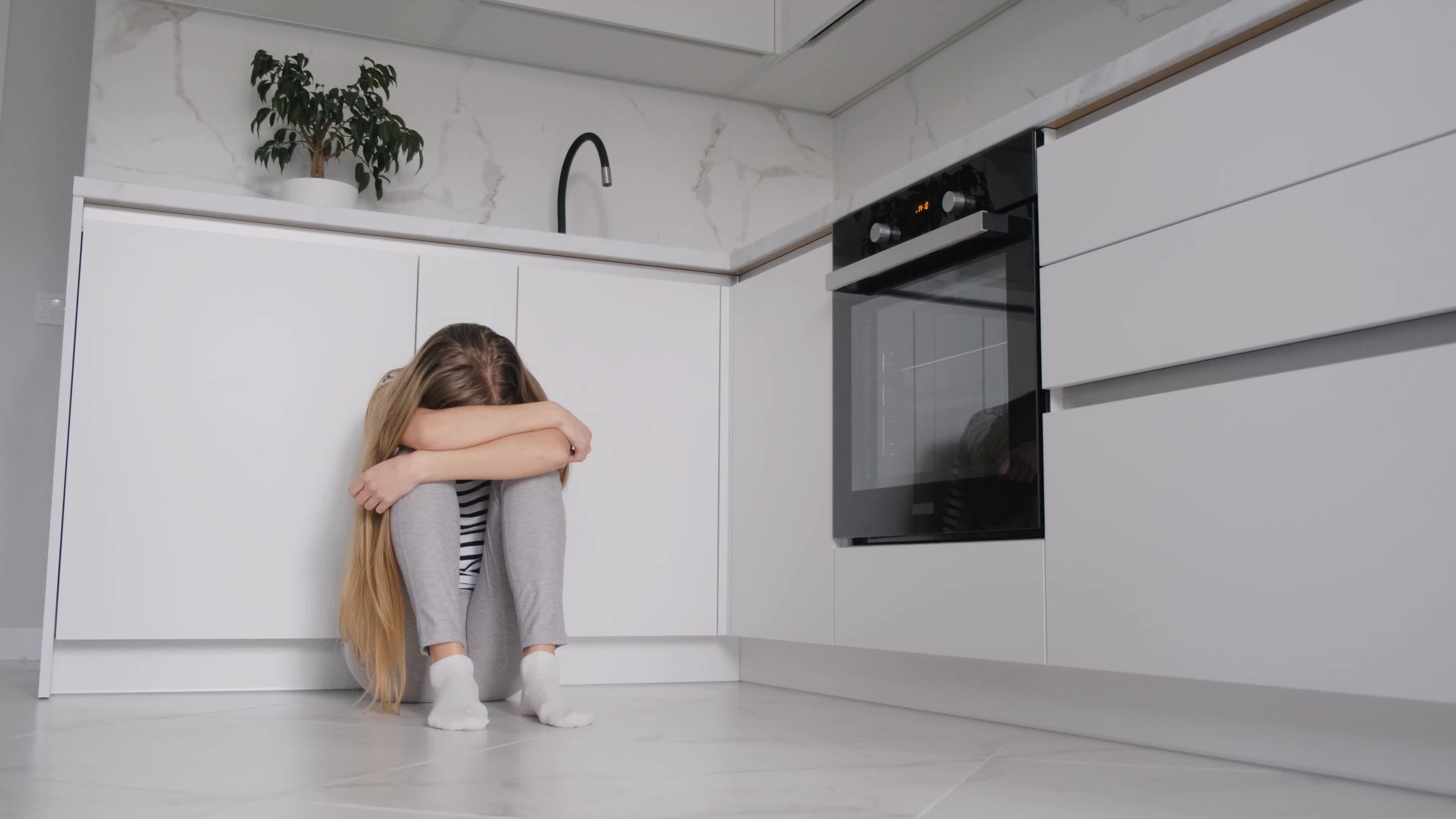 Une femme photographiée assise sur le sol de la cuisine, la tête cachée entre ses genoux | Source : Shutterstock