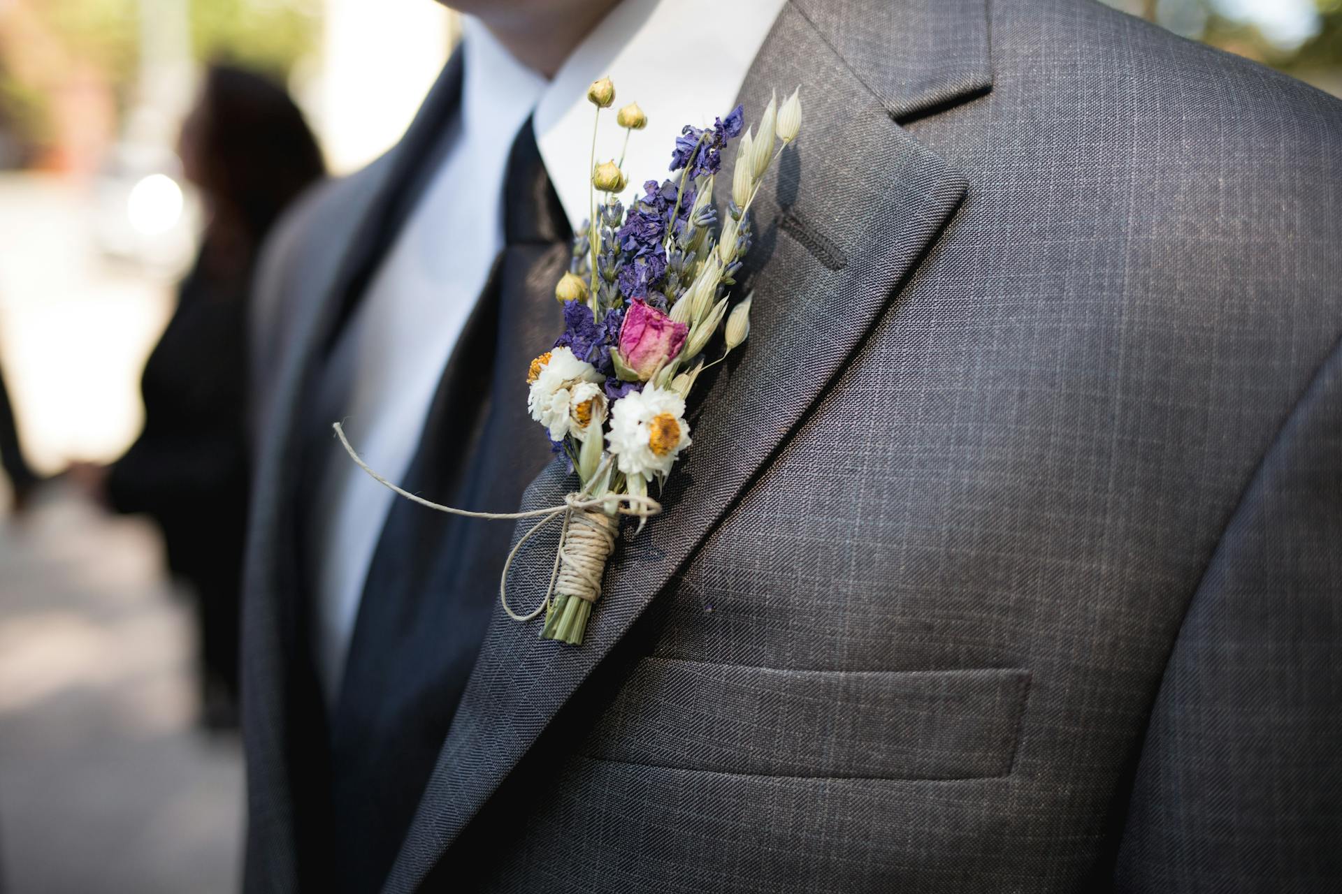 Une boutonnière de fleurs sur la veste de costume grise d'un marié | Source : Pexels