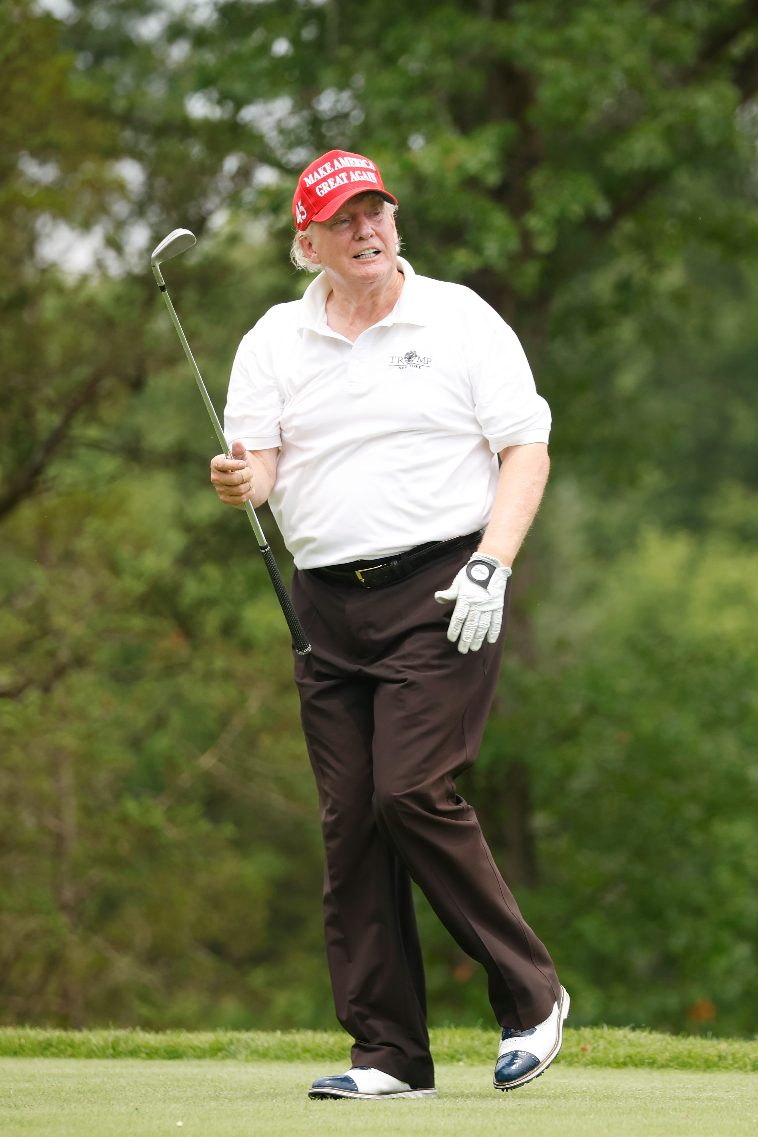 Donald Trump apparaît détendu, tenant un club d'une main tout en souriant légèrement. Les irrégularités de sa peau sont évidentes, en particulier au niveau du menton et des tempes.