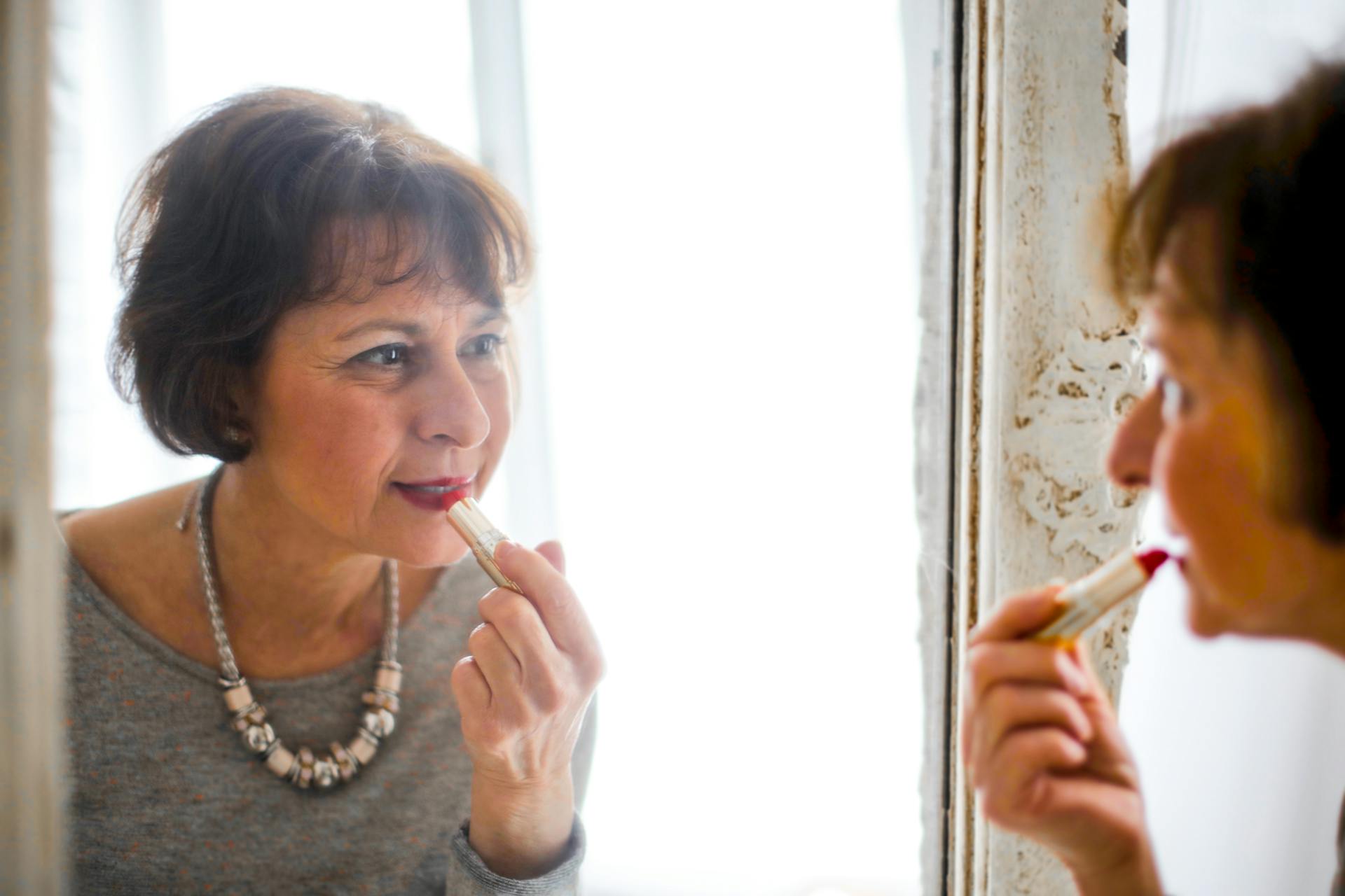 Une femme âgée appliquant du rouge à lèvres devant le miroir | Source : Pexels