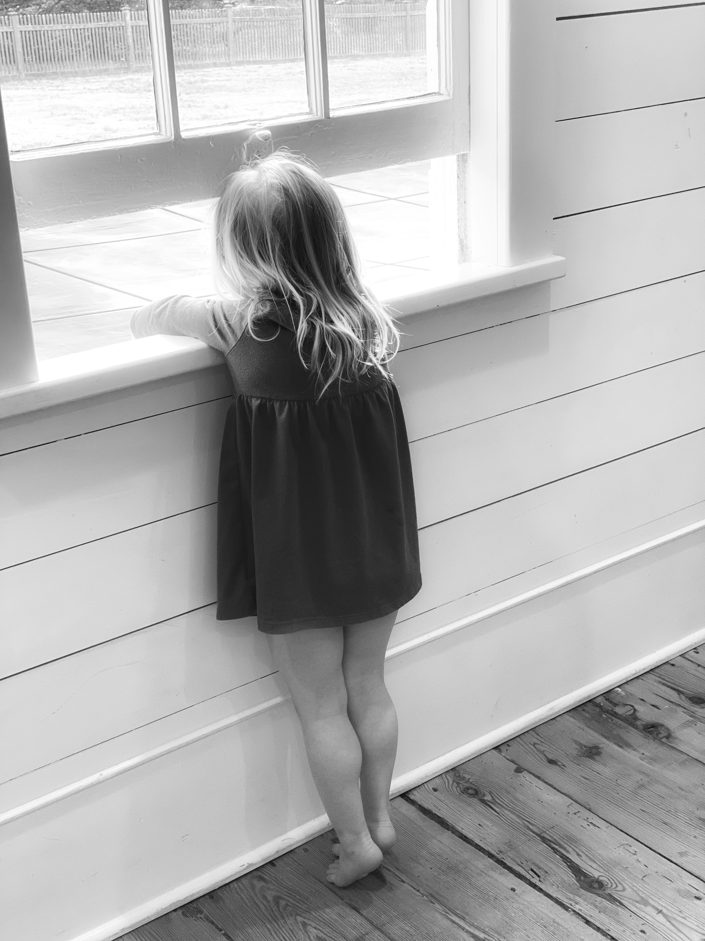 Un cliché en niveaux de gris d'une petite fille debout pieds nus et regardant par la fenêtre | Source : Unsplash