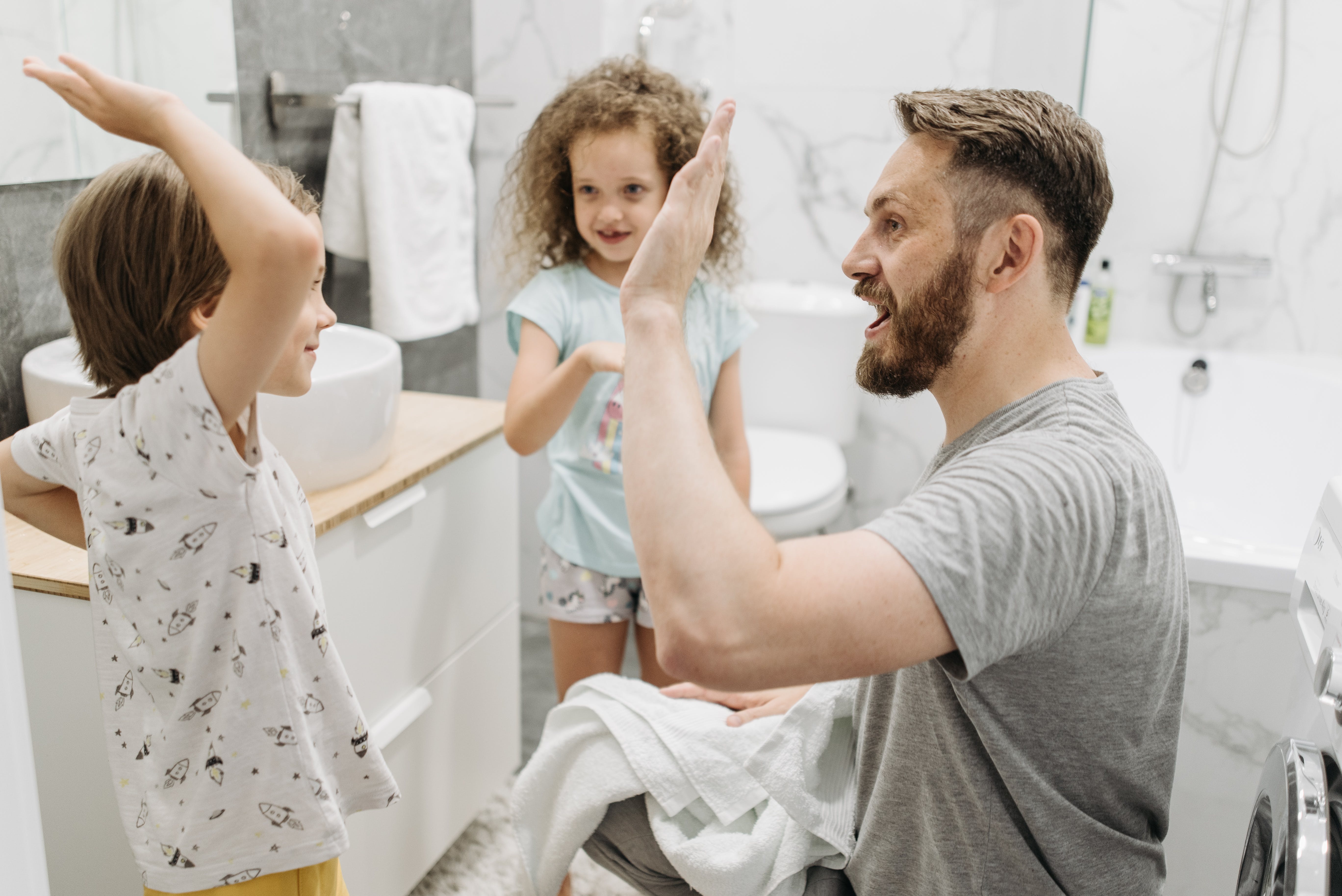 Un homme fait un high-five à un enfant tandis qu'une autre le regarde dans la salle de bain | Source : Pexels