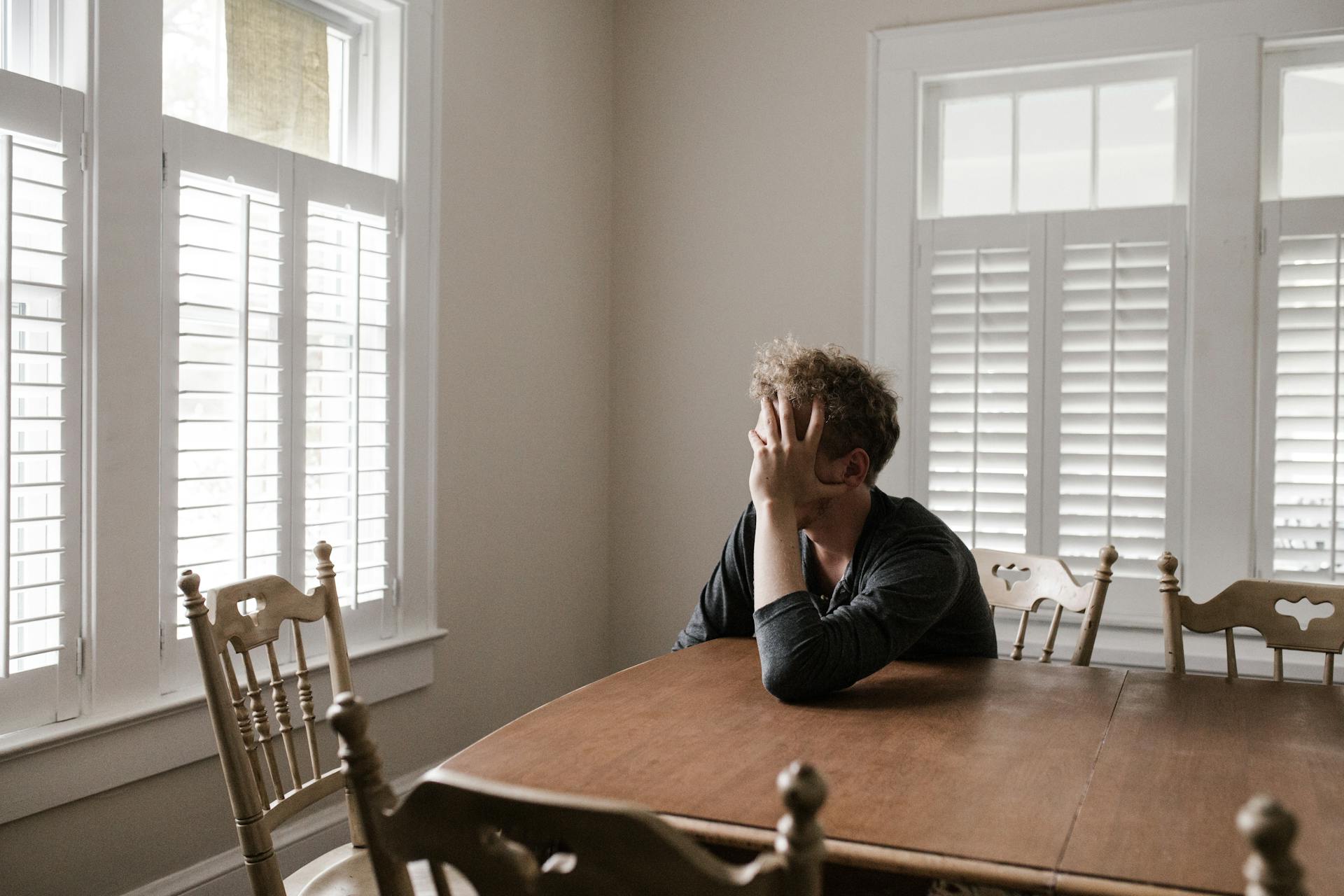 Un jeune homme s'appuie sur une table en bois en se cachant le visage | Source : Pexels