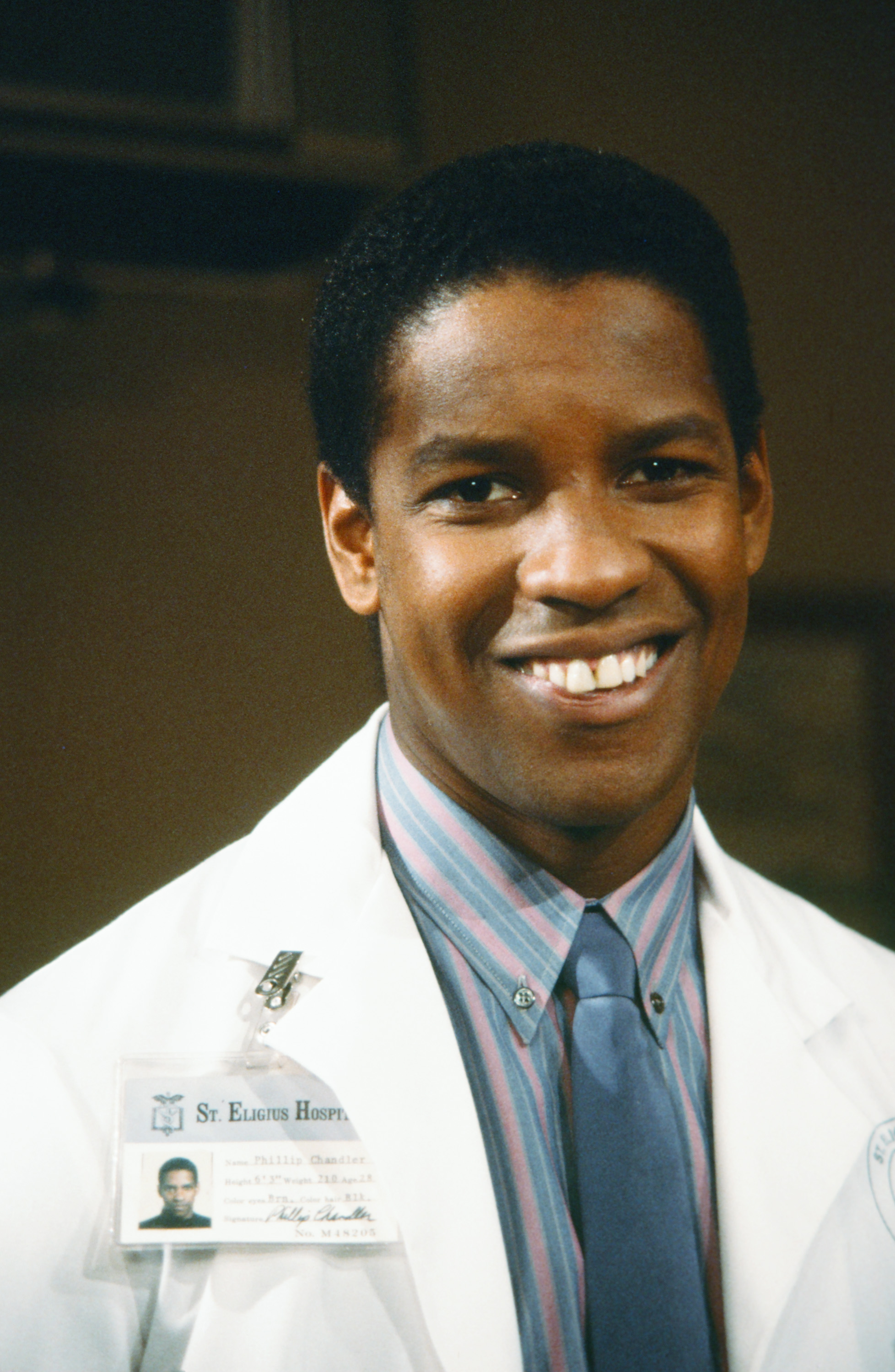 Sur le tournage de « St. Elsewhere », Denzel Washington sourit dans son rôle du Dr Philip Chandler. Son apparence jeune et sa coiffure soignée et naturelle reflètent les débuts de l'acteur dans les séries télévisées.