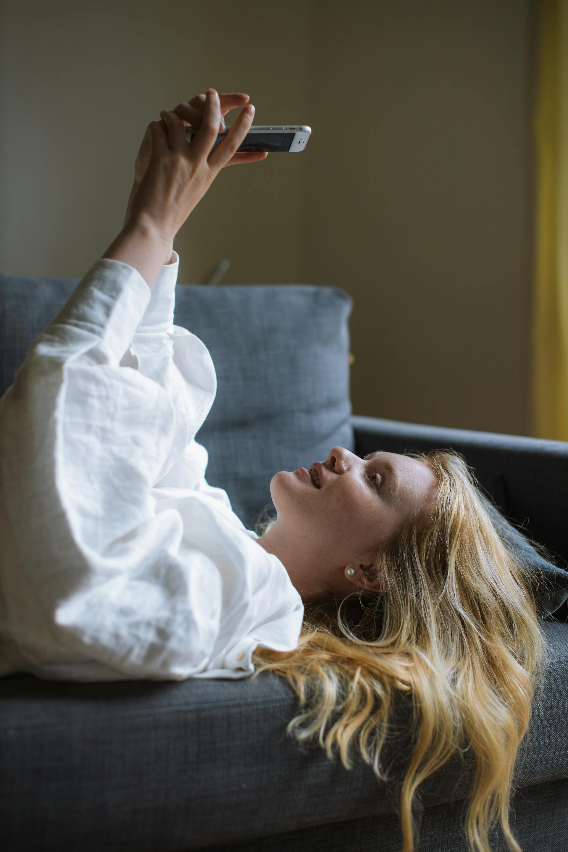 Une jeune femme utilise son téléphone alors qu'elle est allongée sur un canapé | Source : Pexels