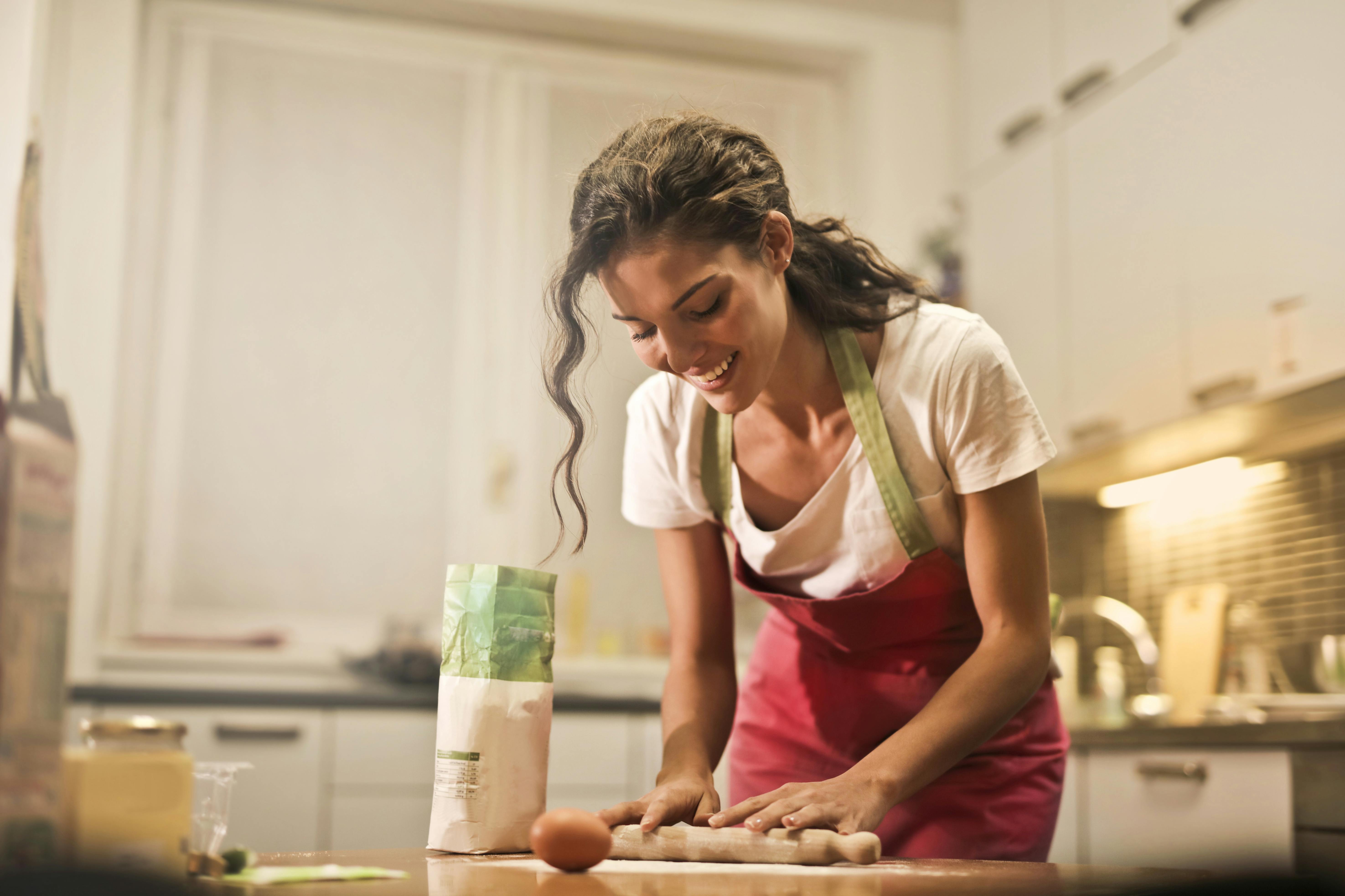 Femme heureuse avec un rouleau à pâtisserie en train de cuisiner à la maison | Source : Pexels