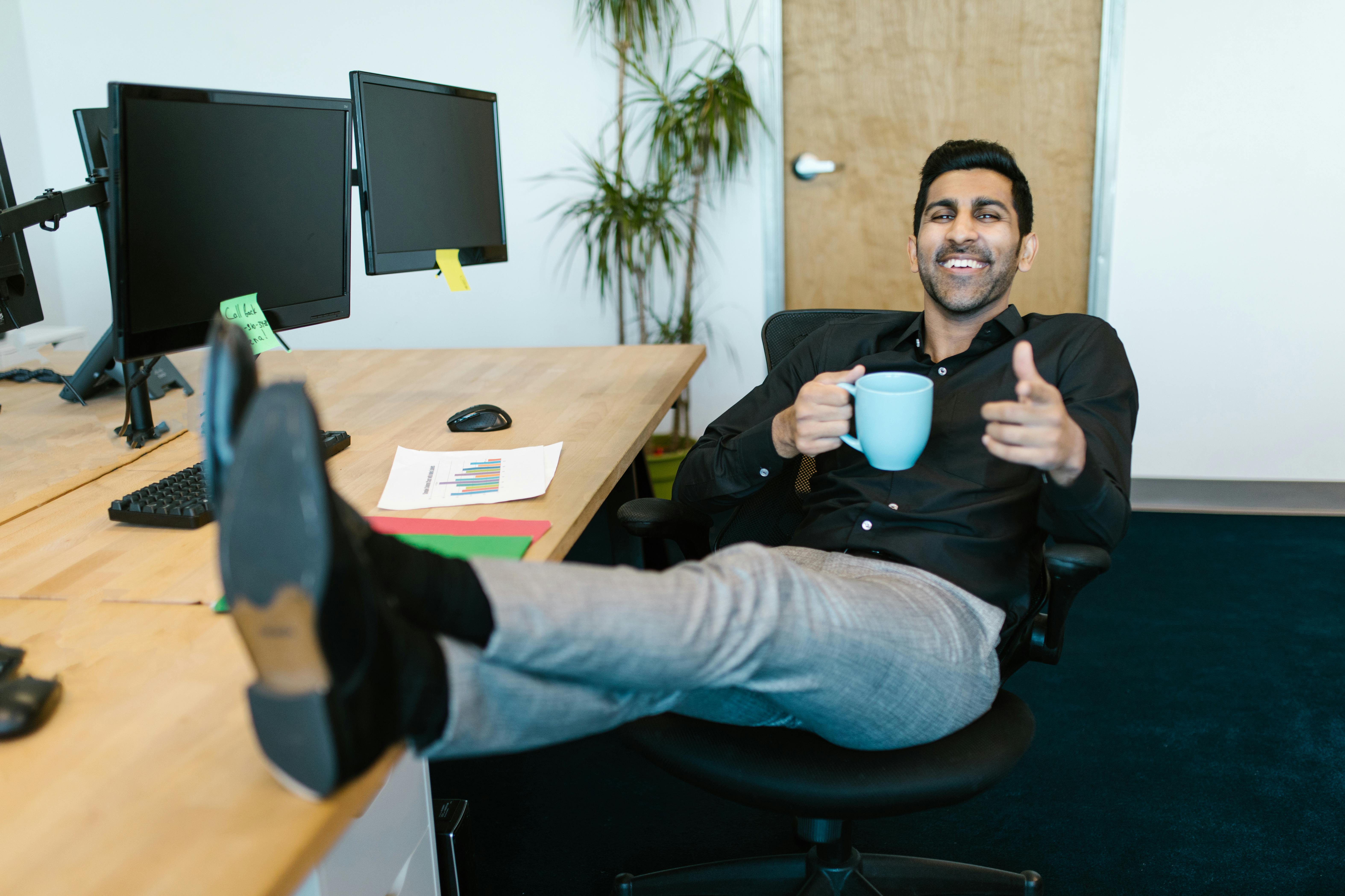 Un homme heureux dégustant une boisson dans son bureau | Source : Pexels