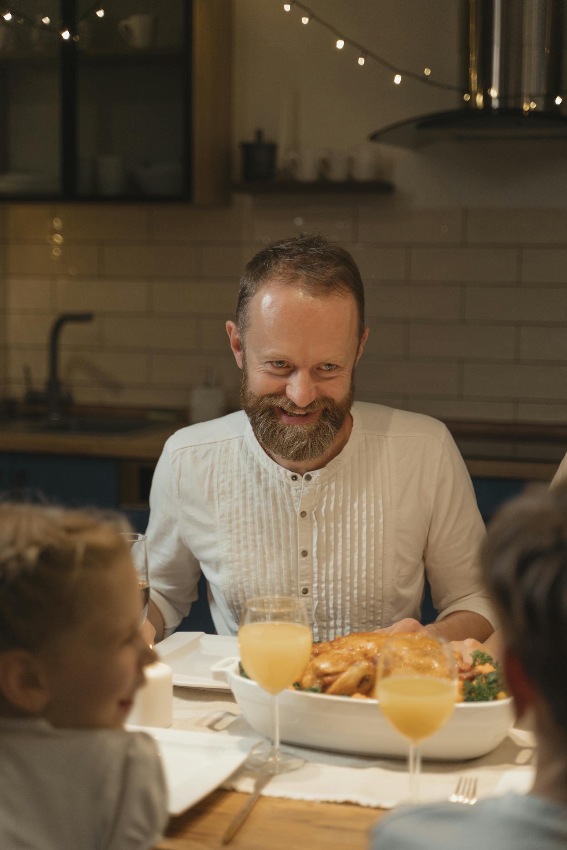 Un homme barbu sourit alors qu'il est assis à la table du dîner | Source : Pexels