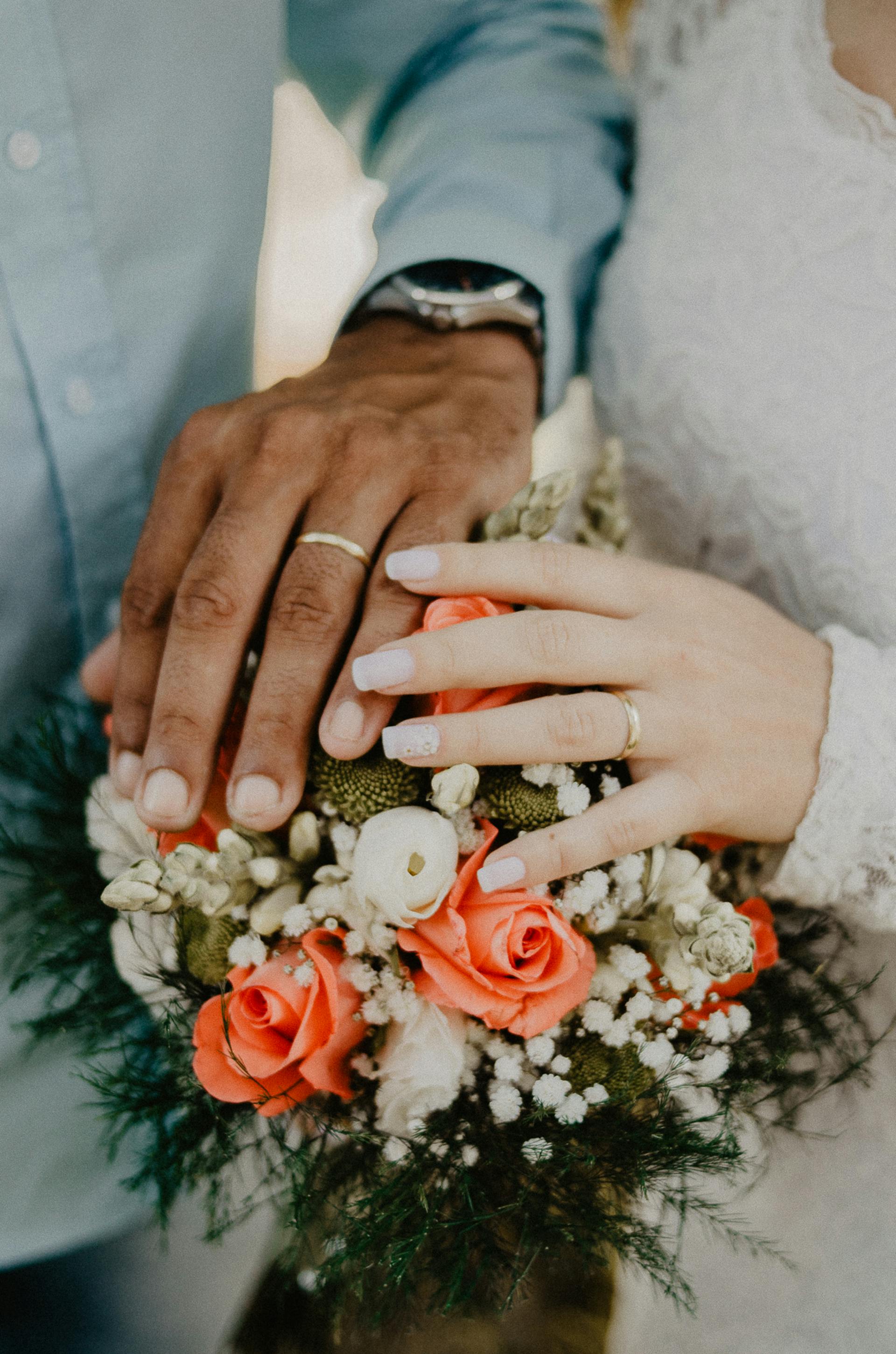 Gros plan sur les mains d'une mariée et d'un marié au-dessus d'un bouquet | Source : Pexels