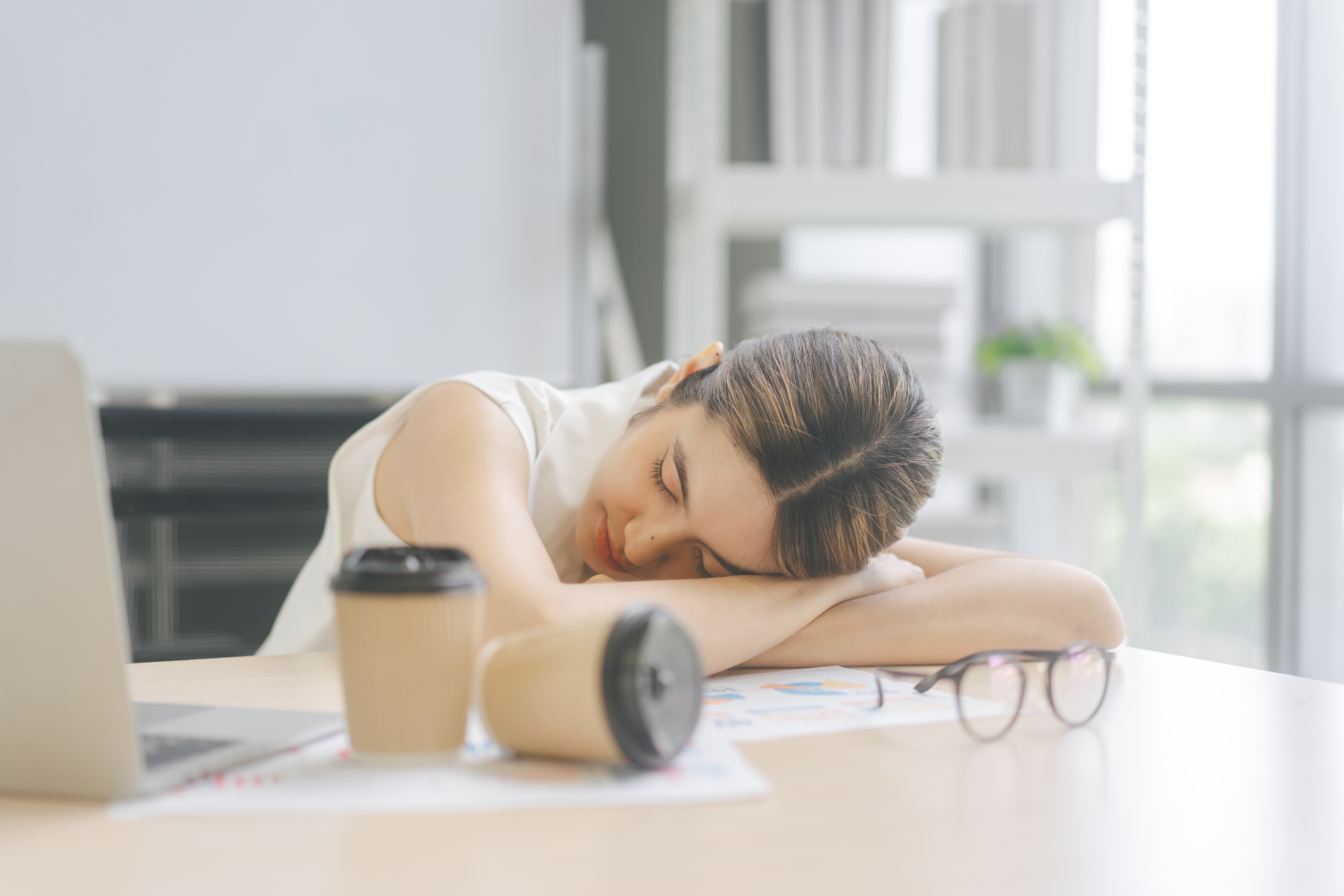 Une jeune femme fatiguée dort sur la table avec des tasses de café | Source : Shutterstock