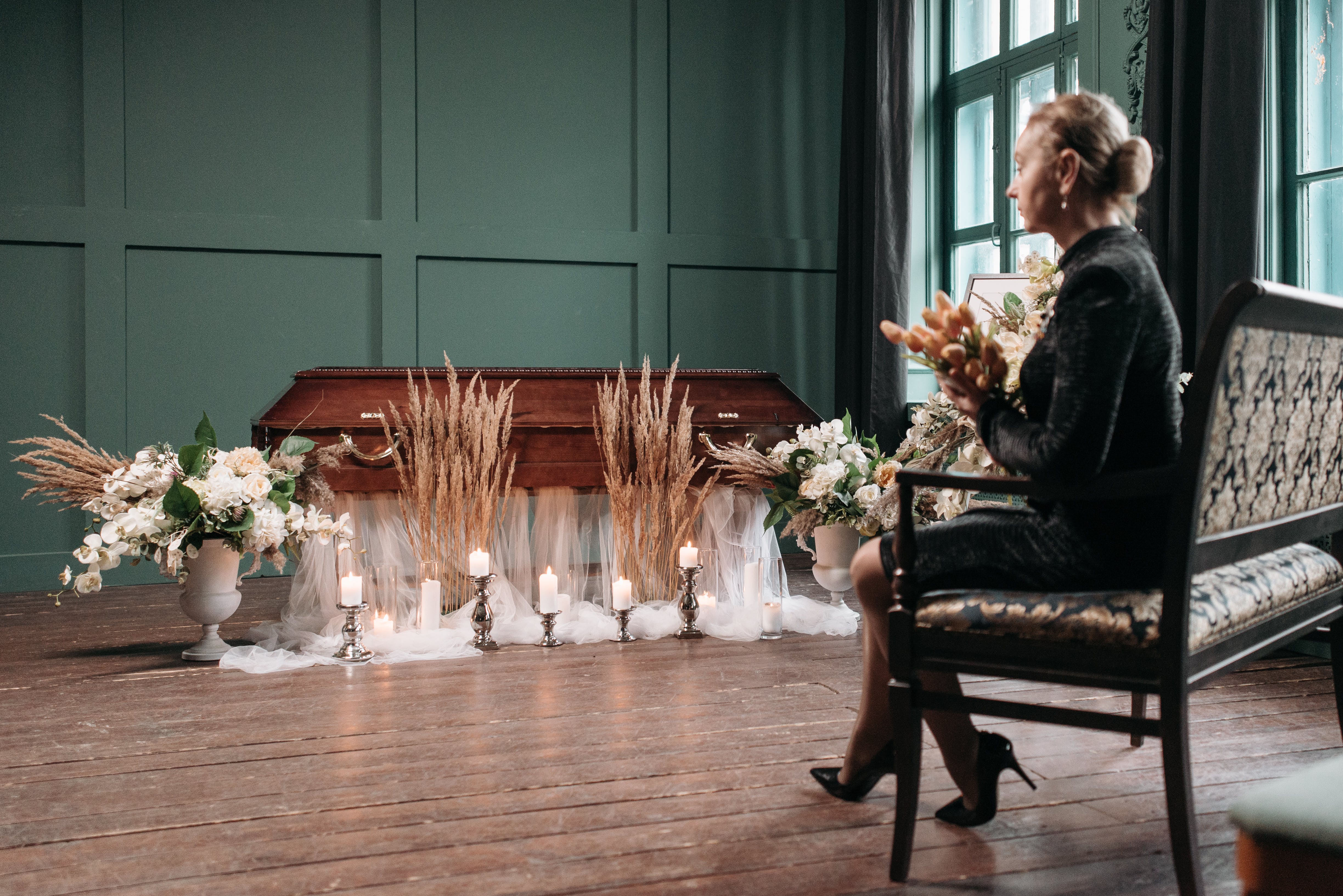 Une femme assise, fleurs à la main, regarde un cercueil | Source : Pexels