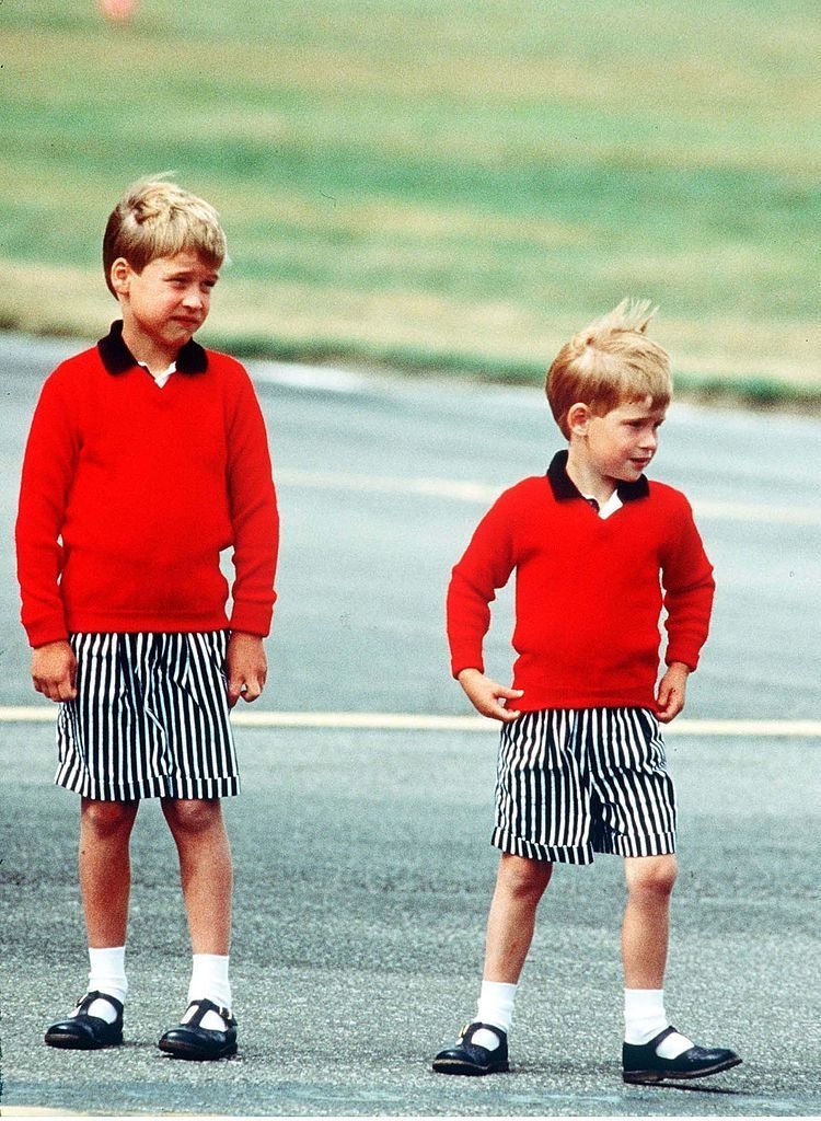 Le prince William et le prince Harry, portant des chandails rouges identiques et des shorts rayés, arrivent à l'aéroport d'Aberdeen. | Source : Getty Images