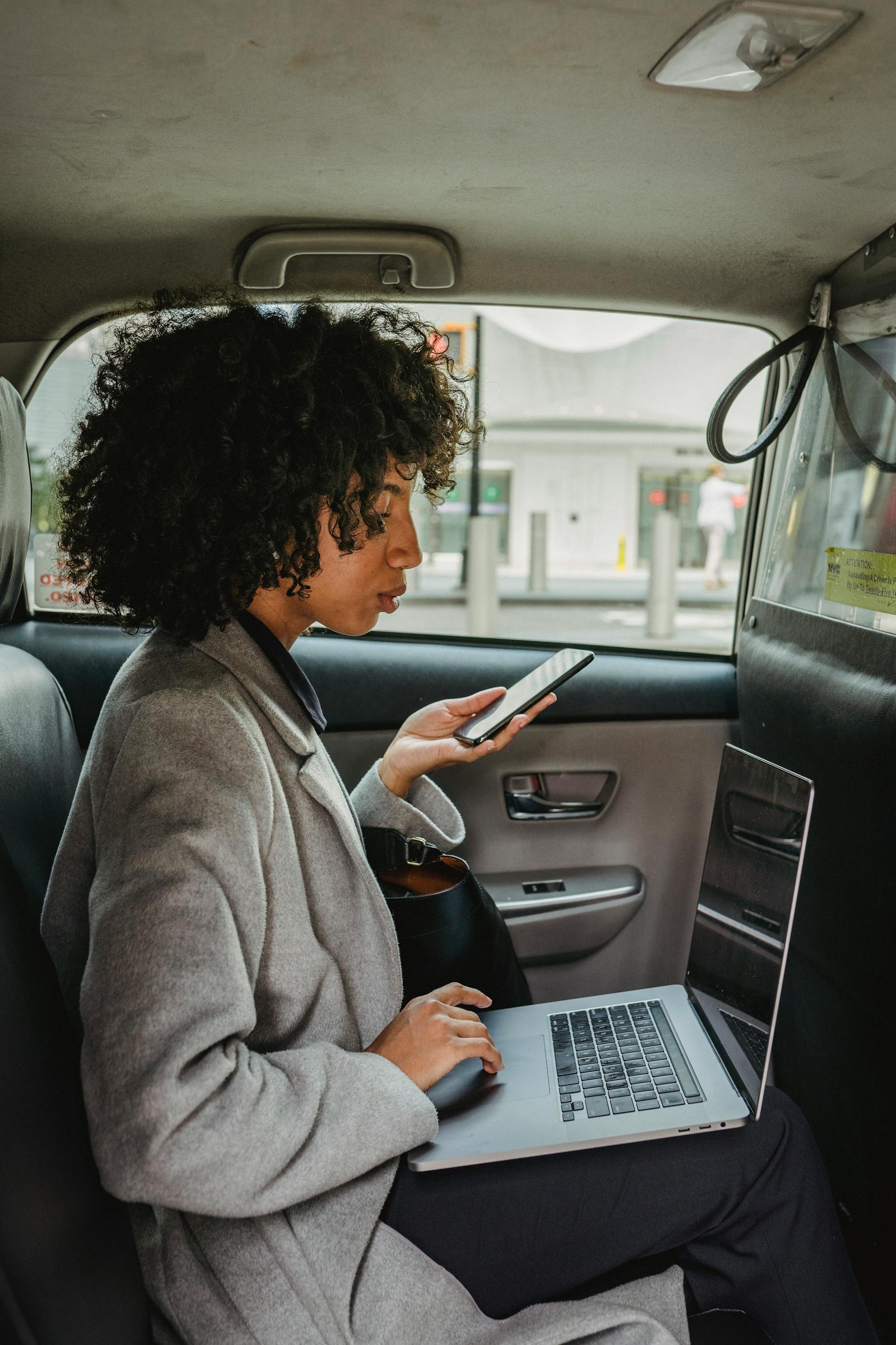 Une femme sérieuse tenant un téléphone et utilisant un ordinateur portable | Source : Pexels