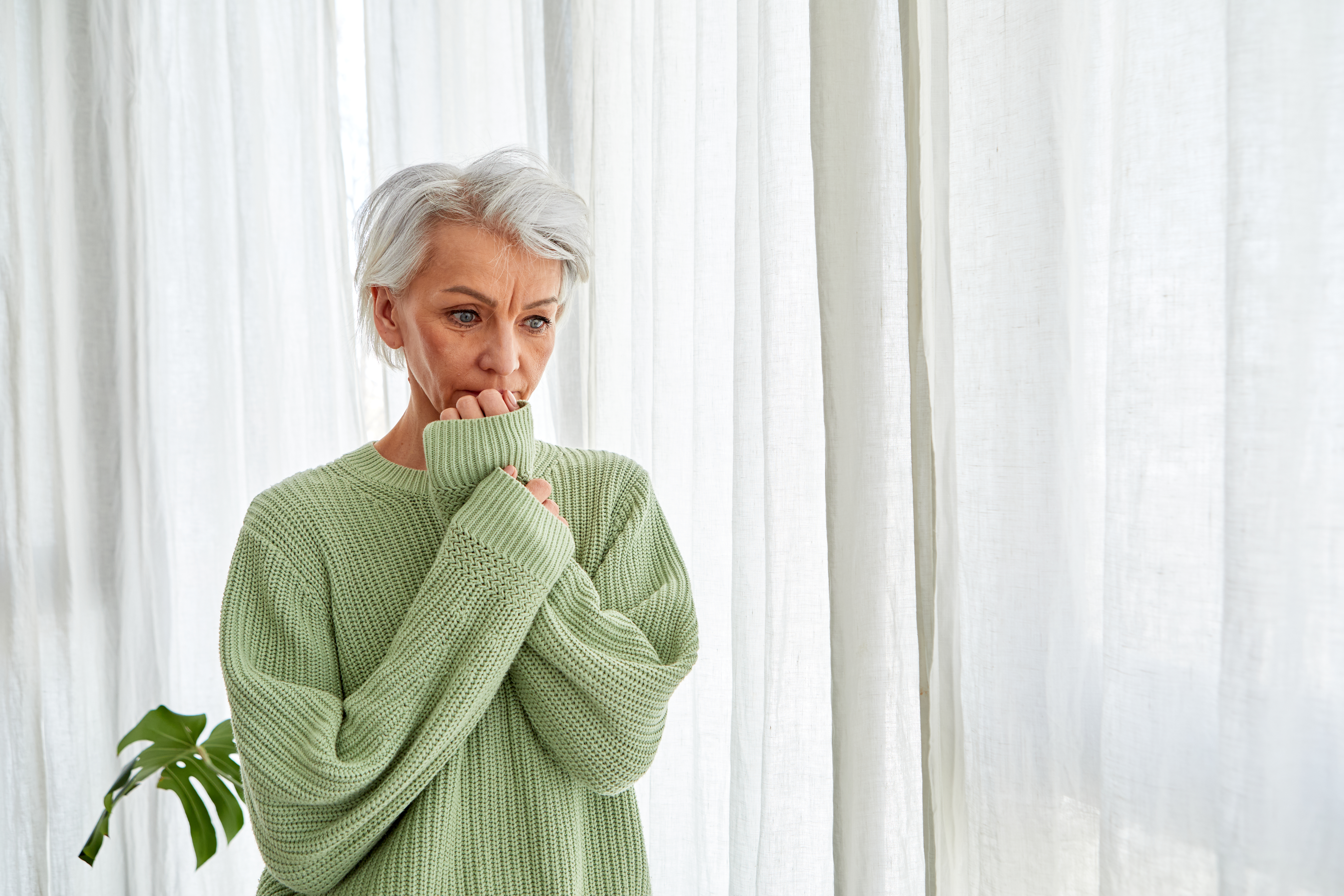 Une femme aux cheveux gris se ronge nerveusement les ongles à la fenêtre | Source : Getty Images