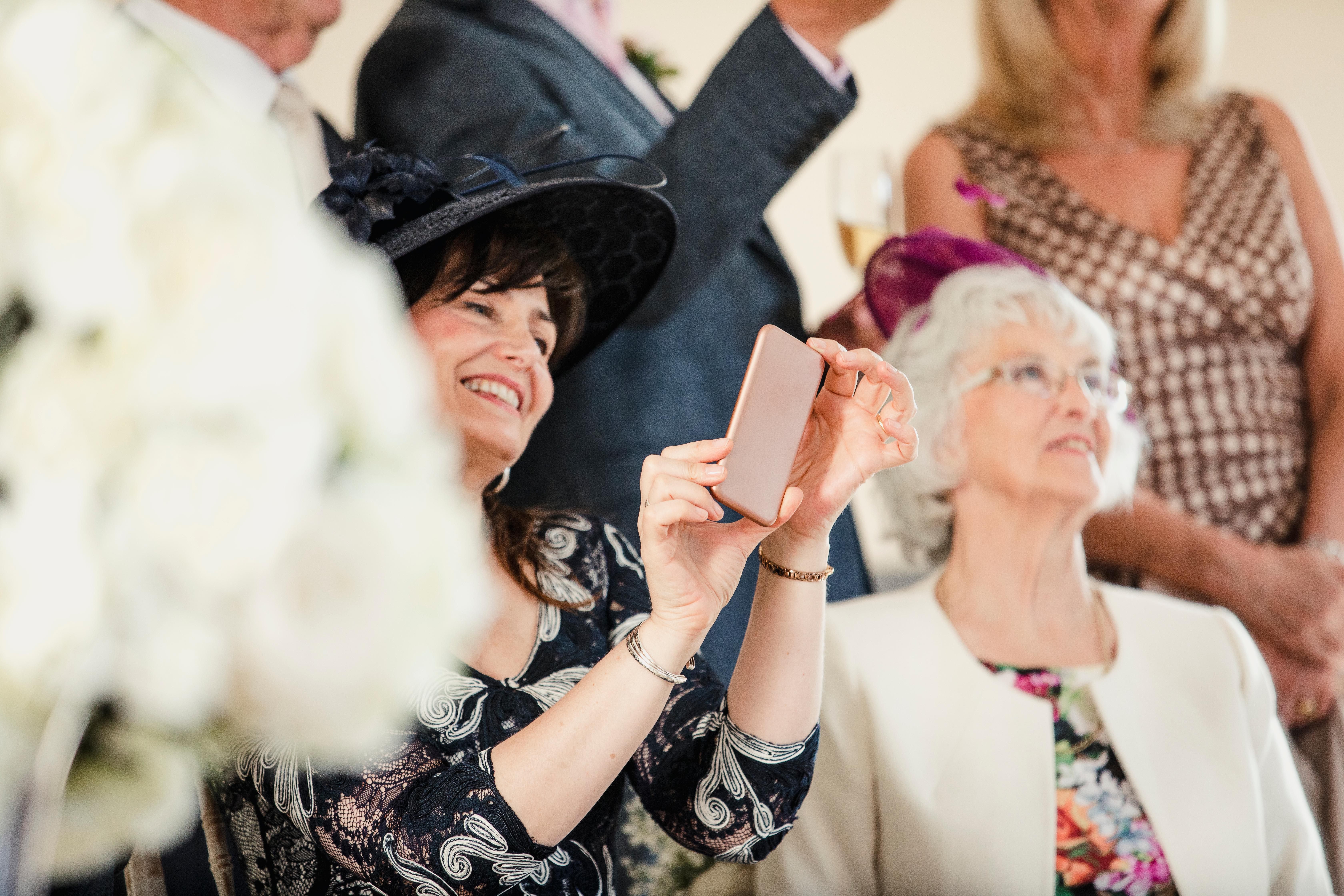 Une femme d'âge moyen est vue tenant un téléphone alors qu'elle est assise à côté d'une dame plus âgée lors d'une cérémonie de mariage | Source : Shutterstock