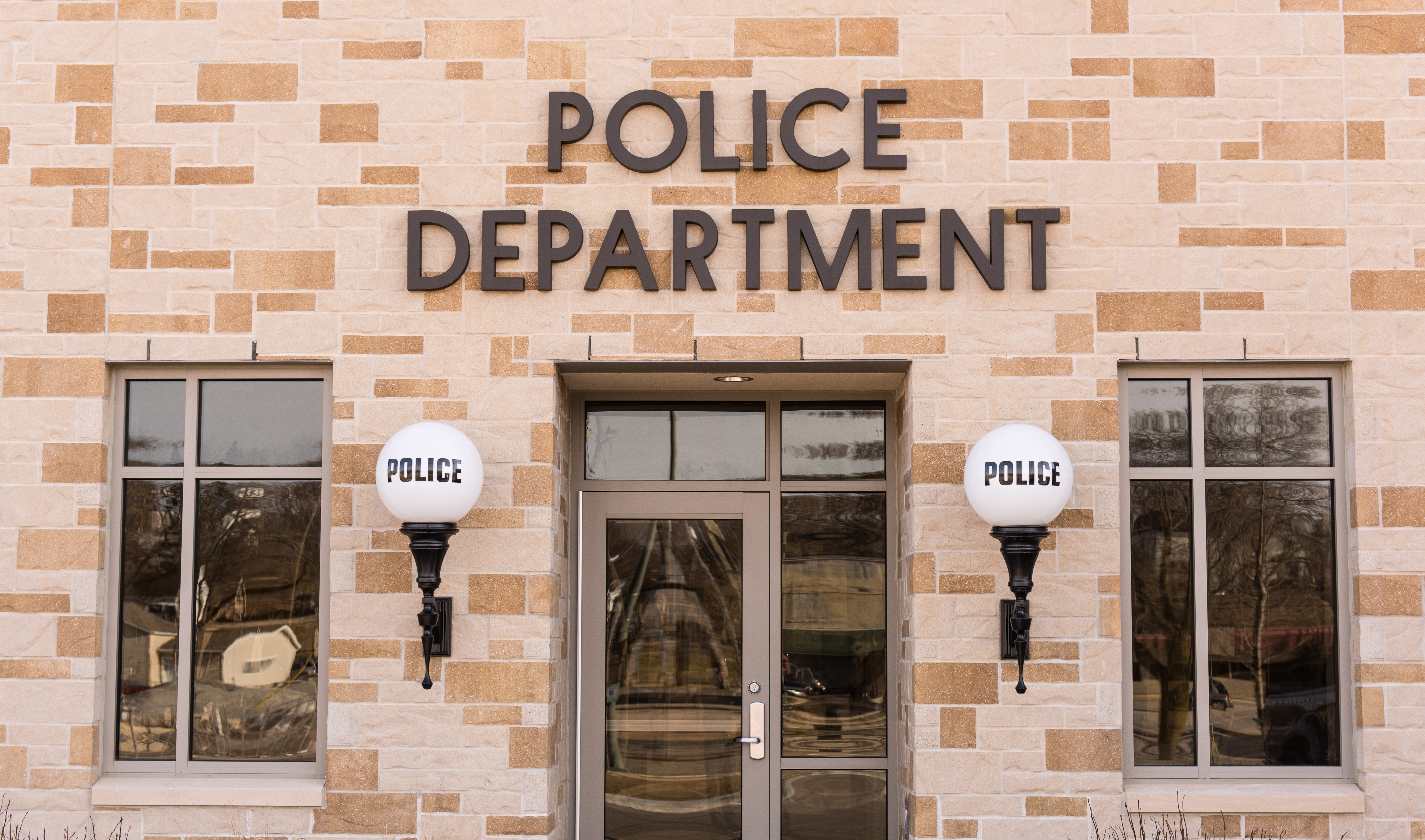 Foto de uma delegacia de polícia com luzes em ambos os lados da porta que indicam polícia.  |  Fonte: Shutterstock