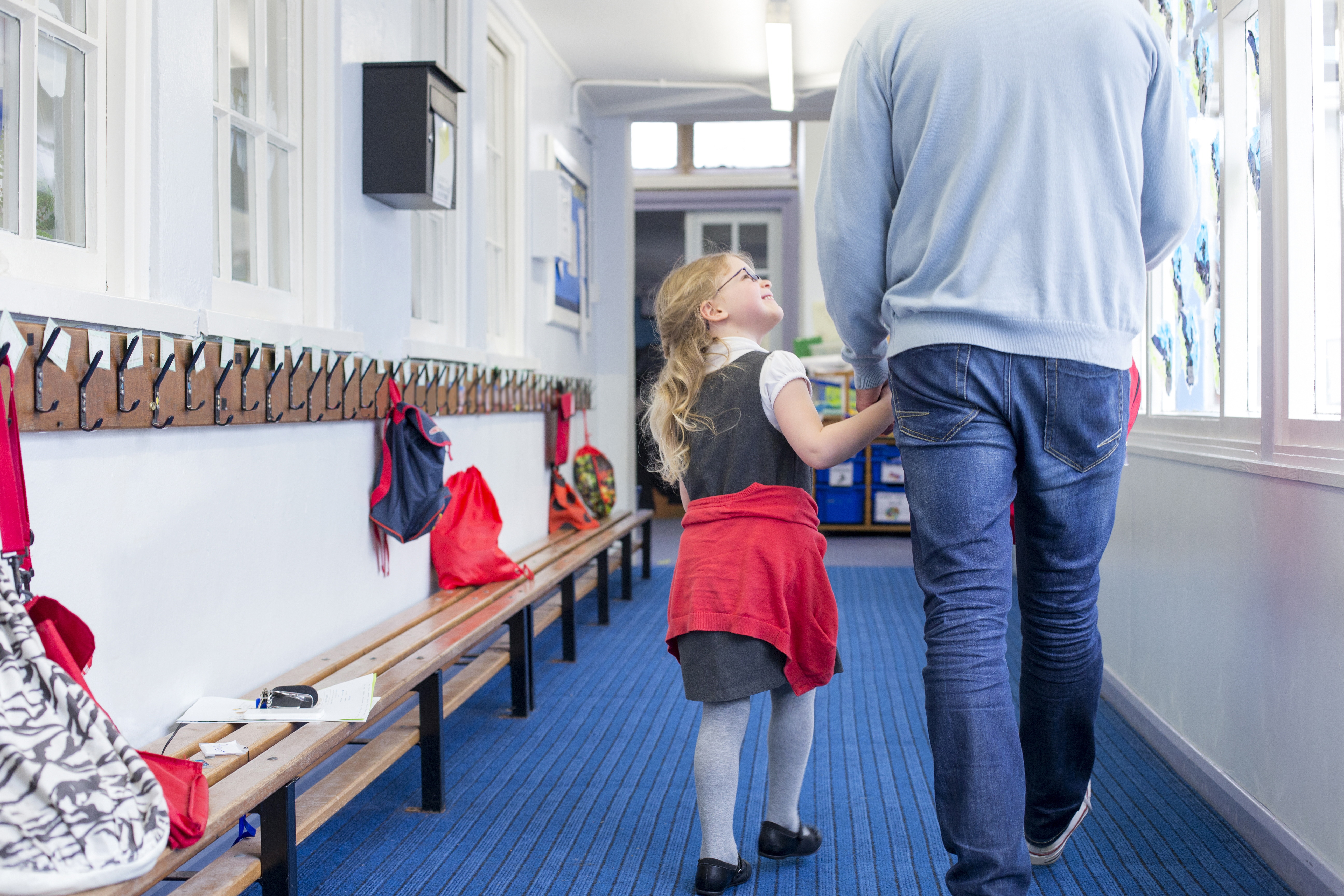 Petite fille souriant et tenant la main d'un homme alors qu'ils marchent dans un couloir | Source : Shutterstock