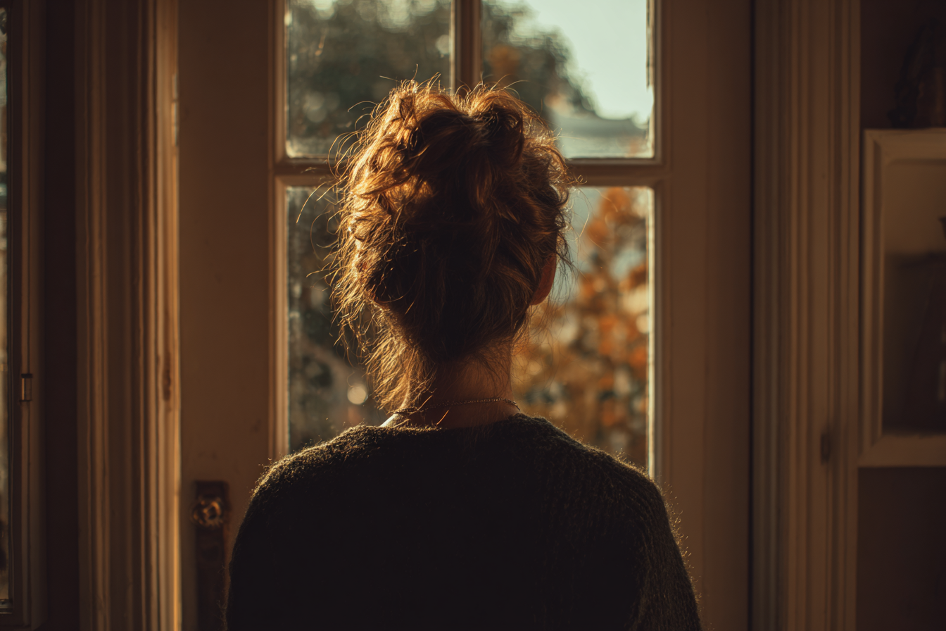 Une femme regardant à l'extérieur d'une fenêtre | Source : Midjourney
