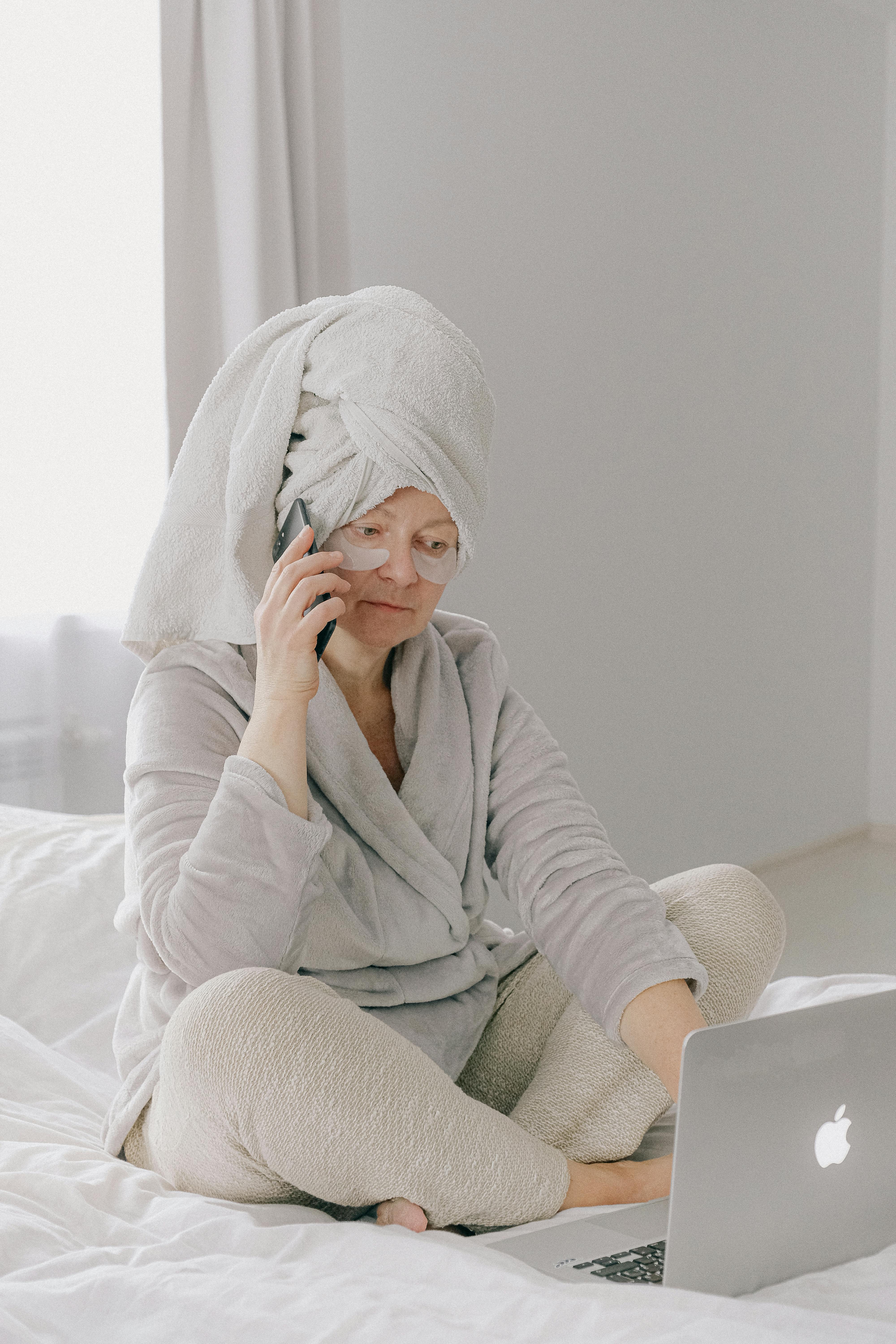 Une femme en robe de chambre et pyjama au téléphone et à l'ordinateur portable | Source : Pexels