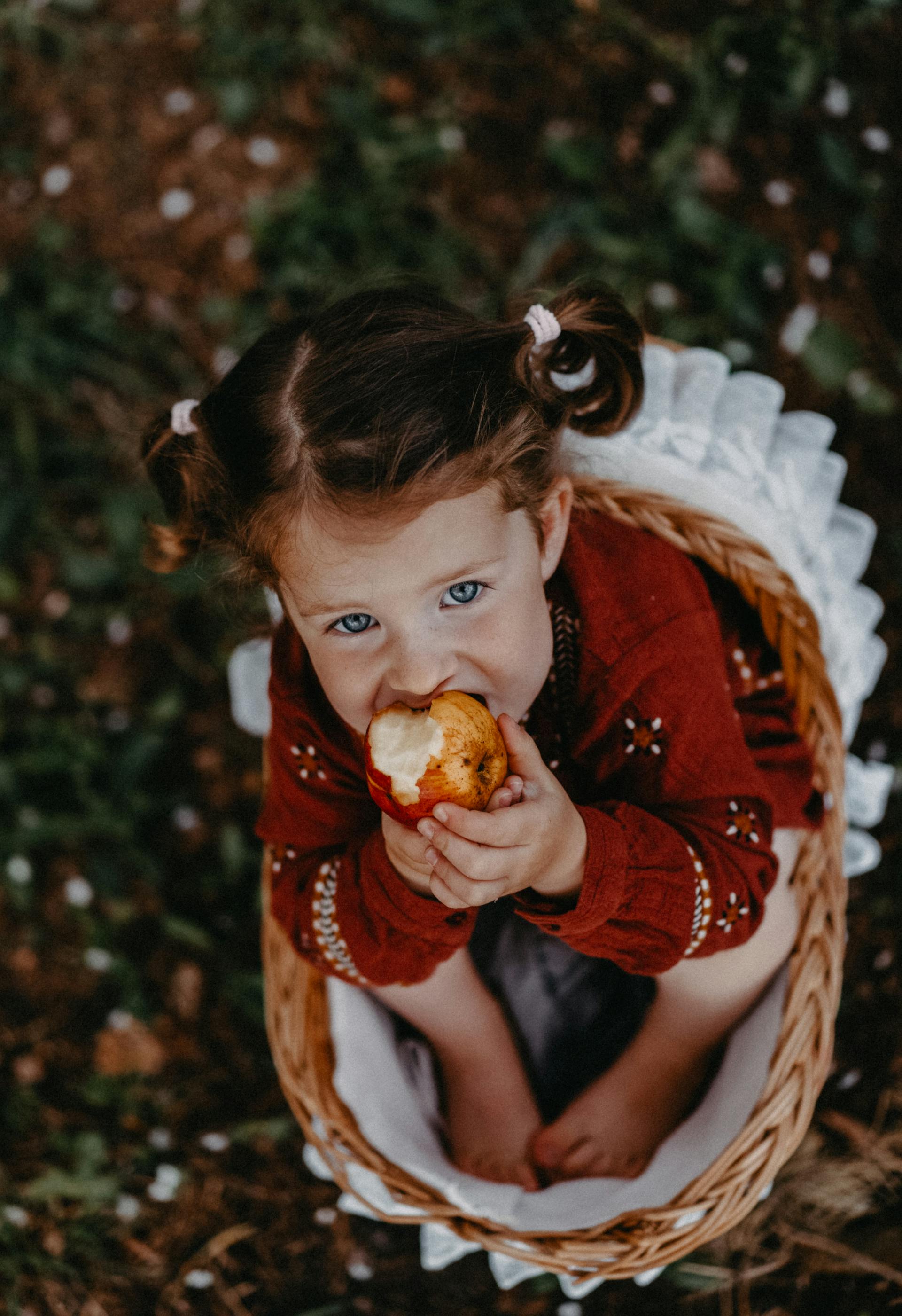 Une fille assise dans un panier mangeant une pomme | Source : Pexels