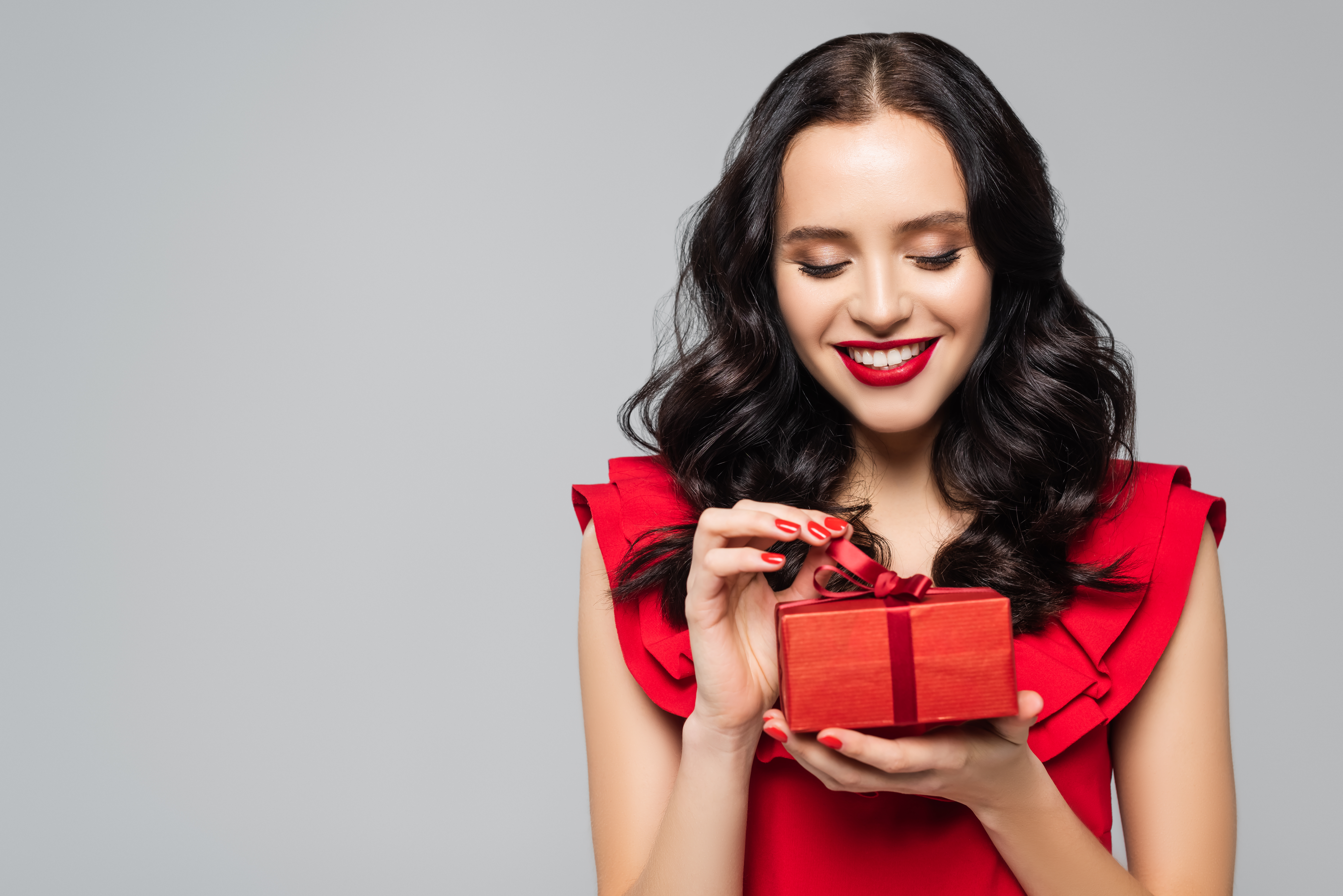 Une femme joyeuse vêtue d'une robe rouge tient un paquet cadeau | Source : Shutterstock