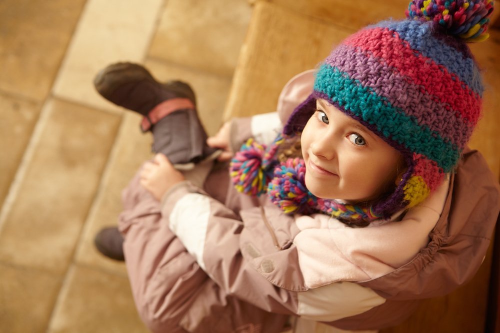 Une fillette souriante enfile ses bottes | Photo: Shutterstock