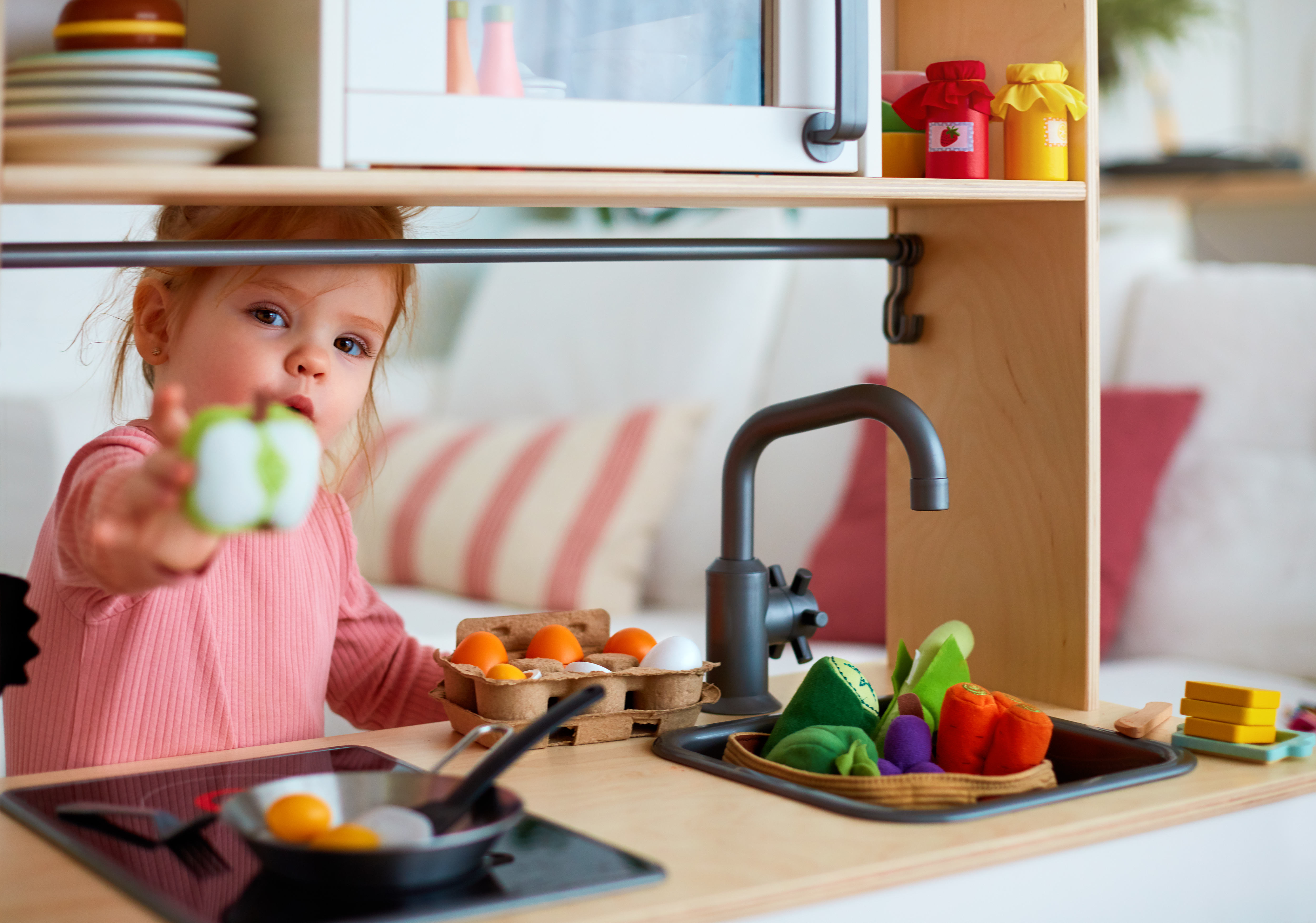 Un enfant tend une pomme en plastique dans une cuisine jouet | Source : Shutterstock