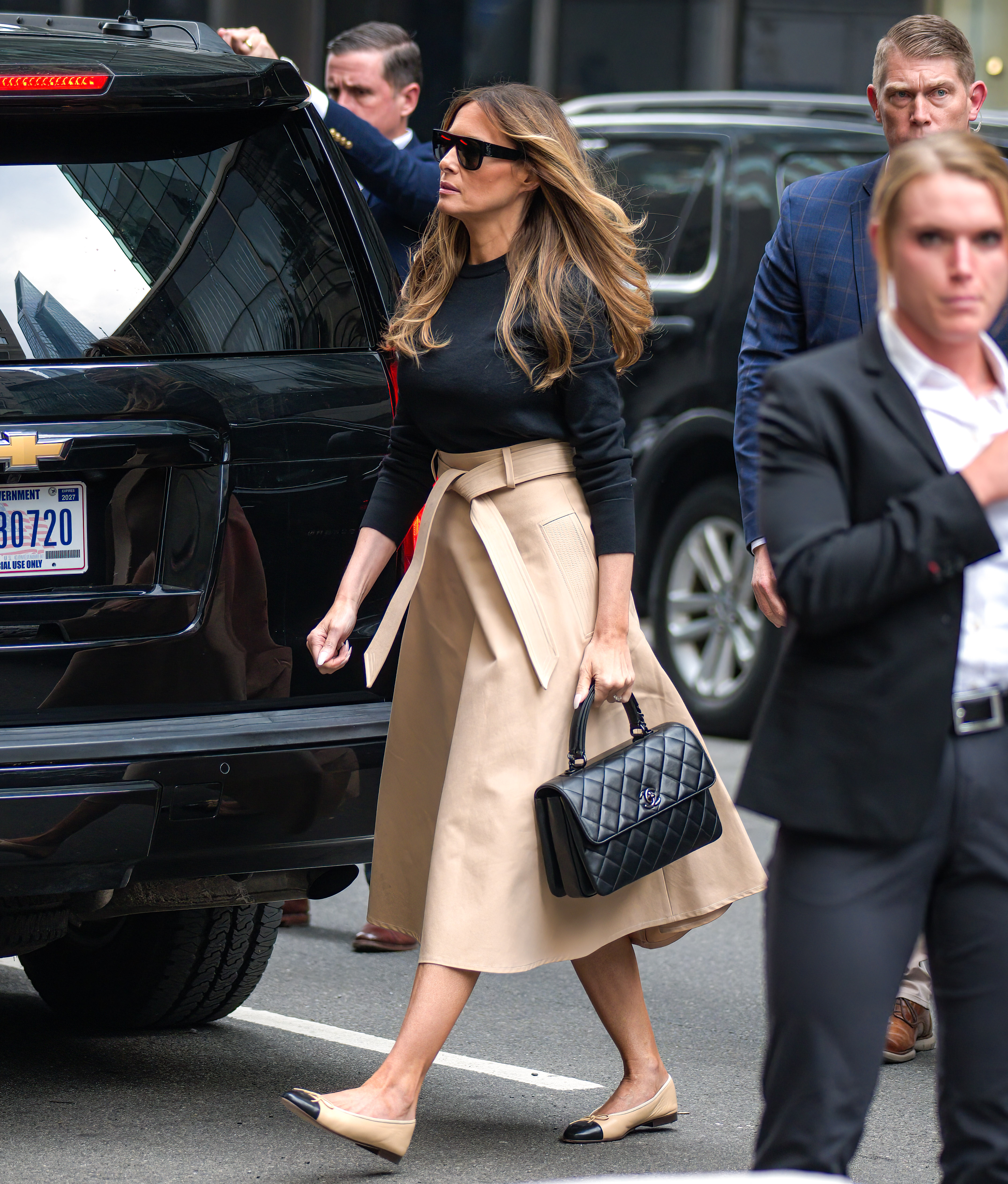 Melania Trump arrive à la Trump Tower à New York le 8 juin 2023, vêtue d'un pull noir à col rond rentré dans une jupe midi à taille haute, ceinture à nouer, le tout agrémenté de lunettes de soleil oversize. Elle complète cette tenue urbaine chic avec un sac à main matelassé Chanel et des ballerines classiques bicolores, beiges et noires, à bout carré.