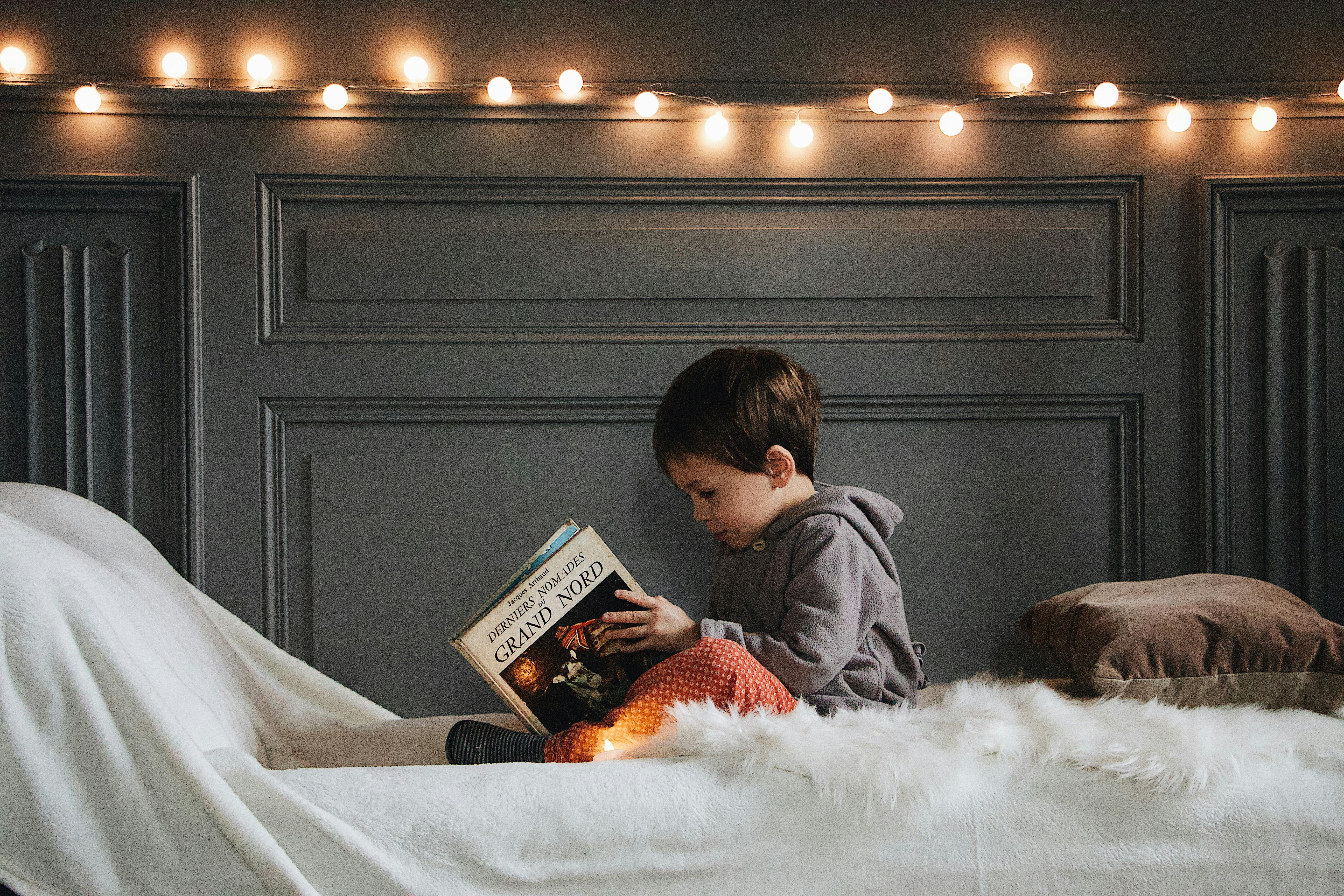 Un petit garçon lisant un livre au lit | Source : Pexels