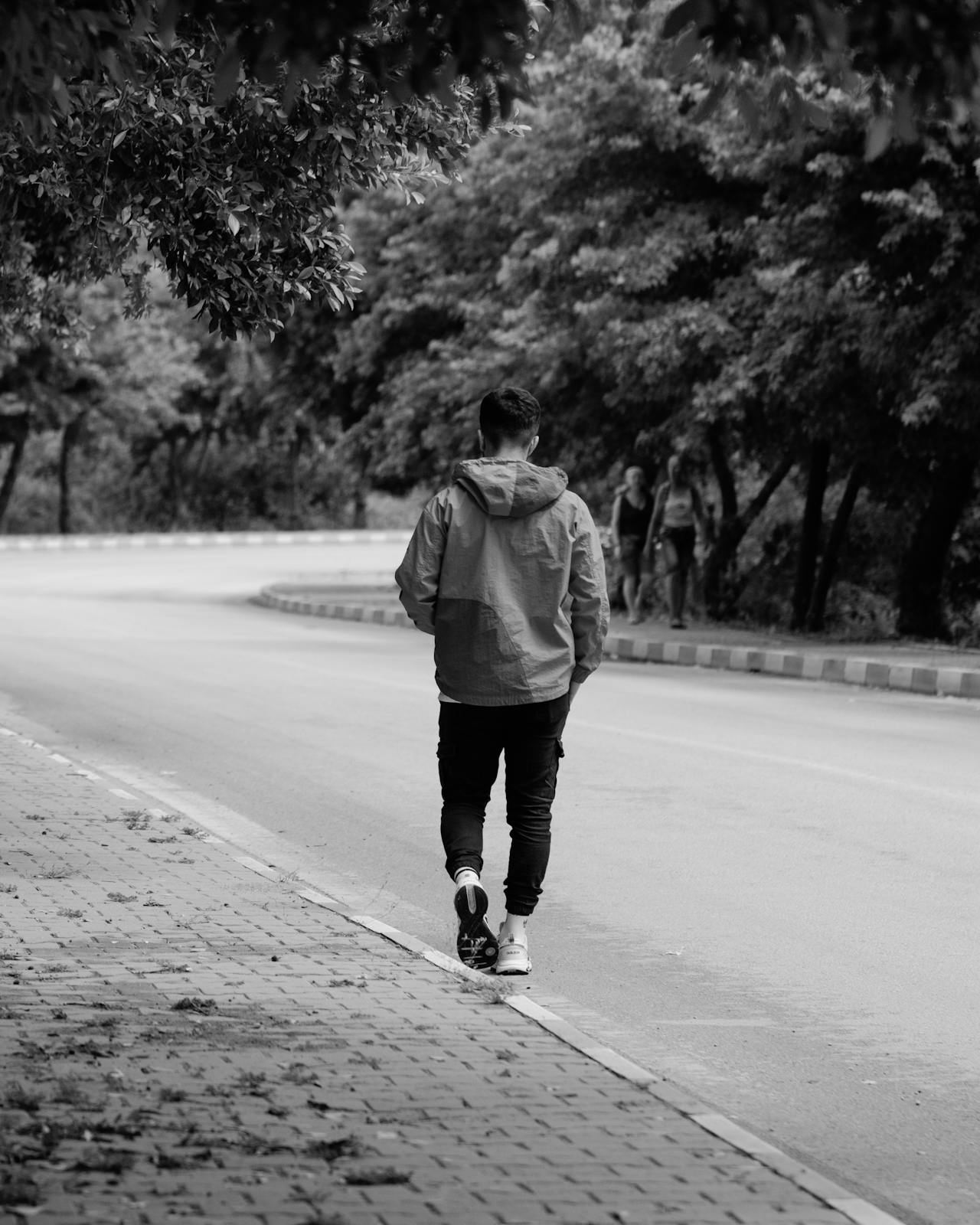 Prise de vue en niveaux de gris d'un jeune homme marchant sur la route | Source : Pexels