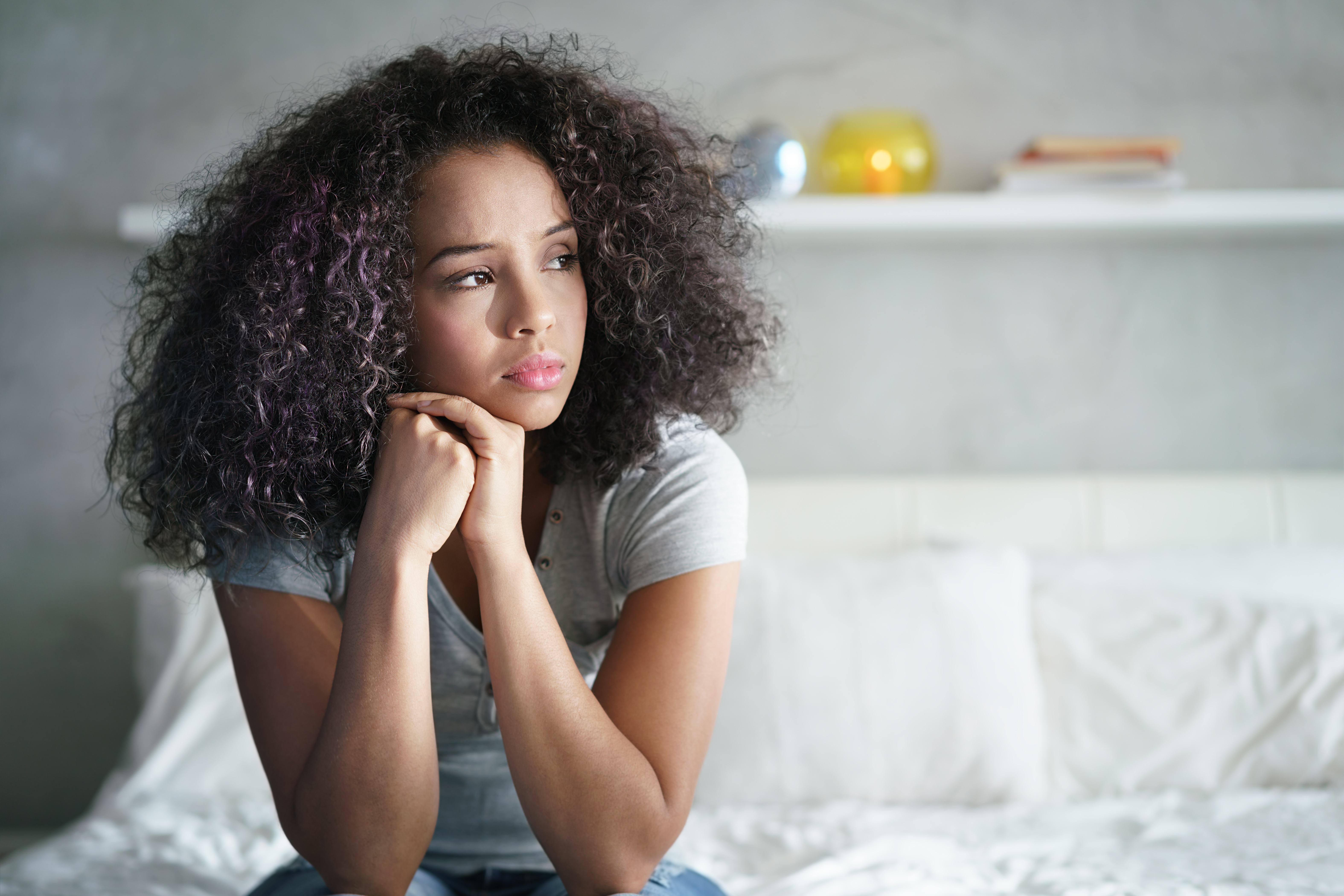 Une femme noire perturbée assise sur un lit le regard ailleurs | Source : Shutterstock
