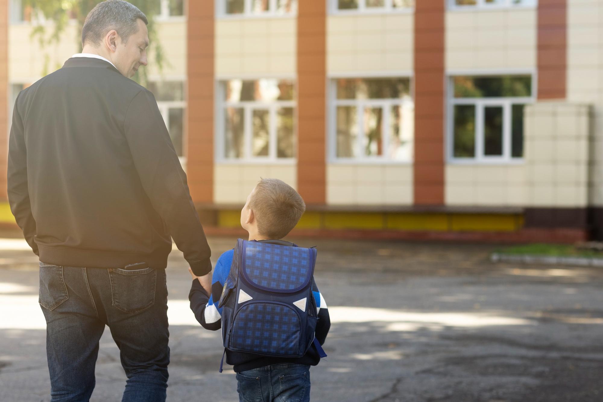 A little boy with a backpack looking at his father | Source: Freepik