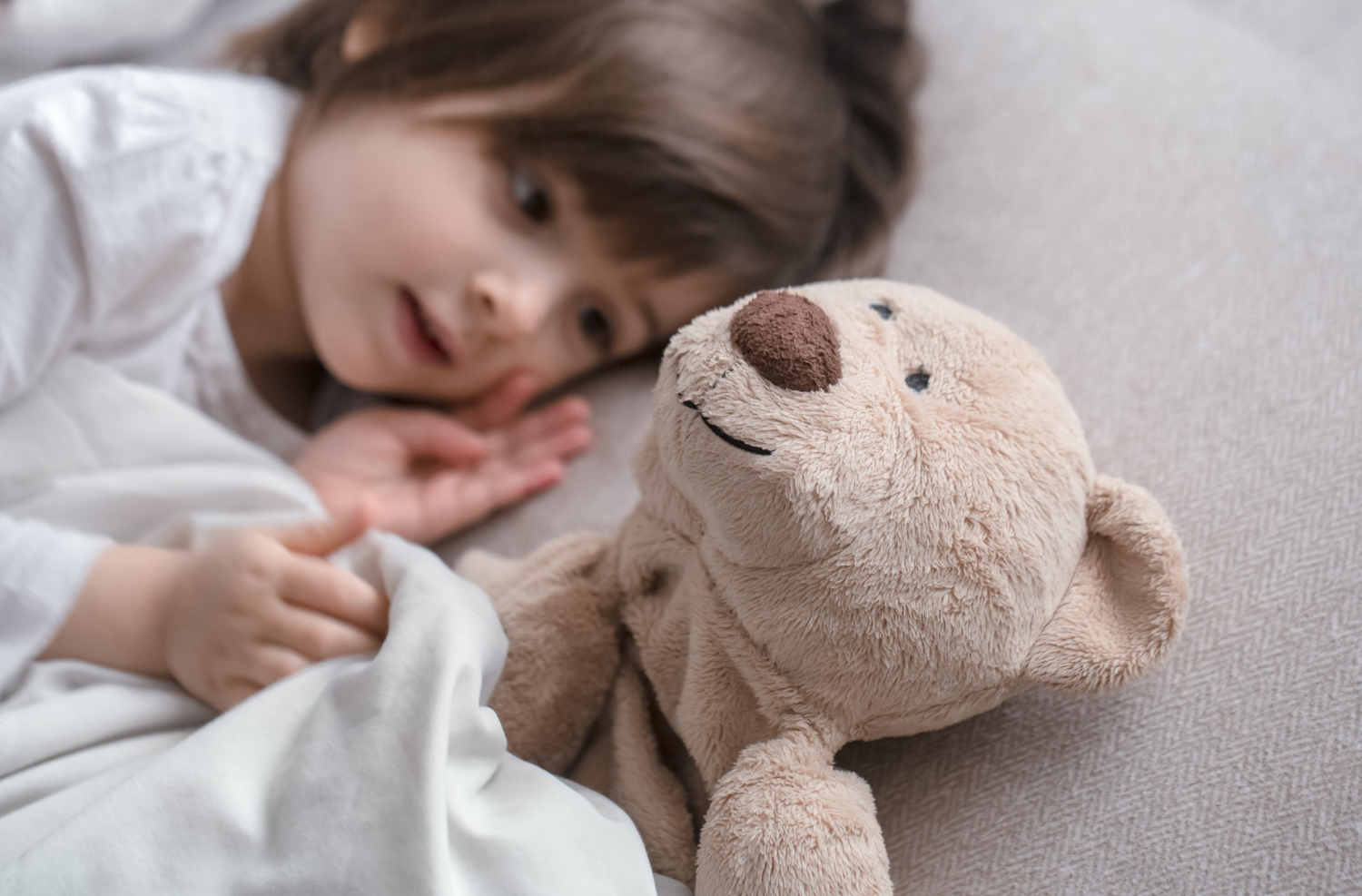 Une petite fille allongée dans son lit à côté de son ours en peluche | Source : Freepik