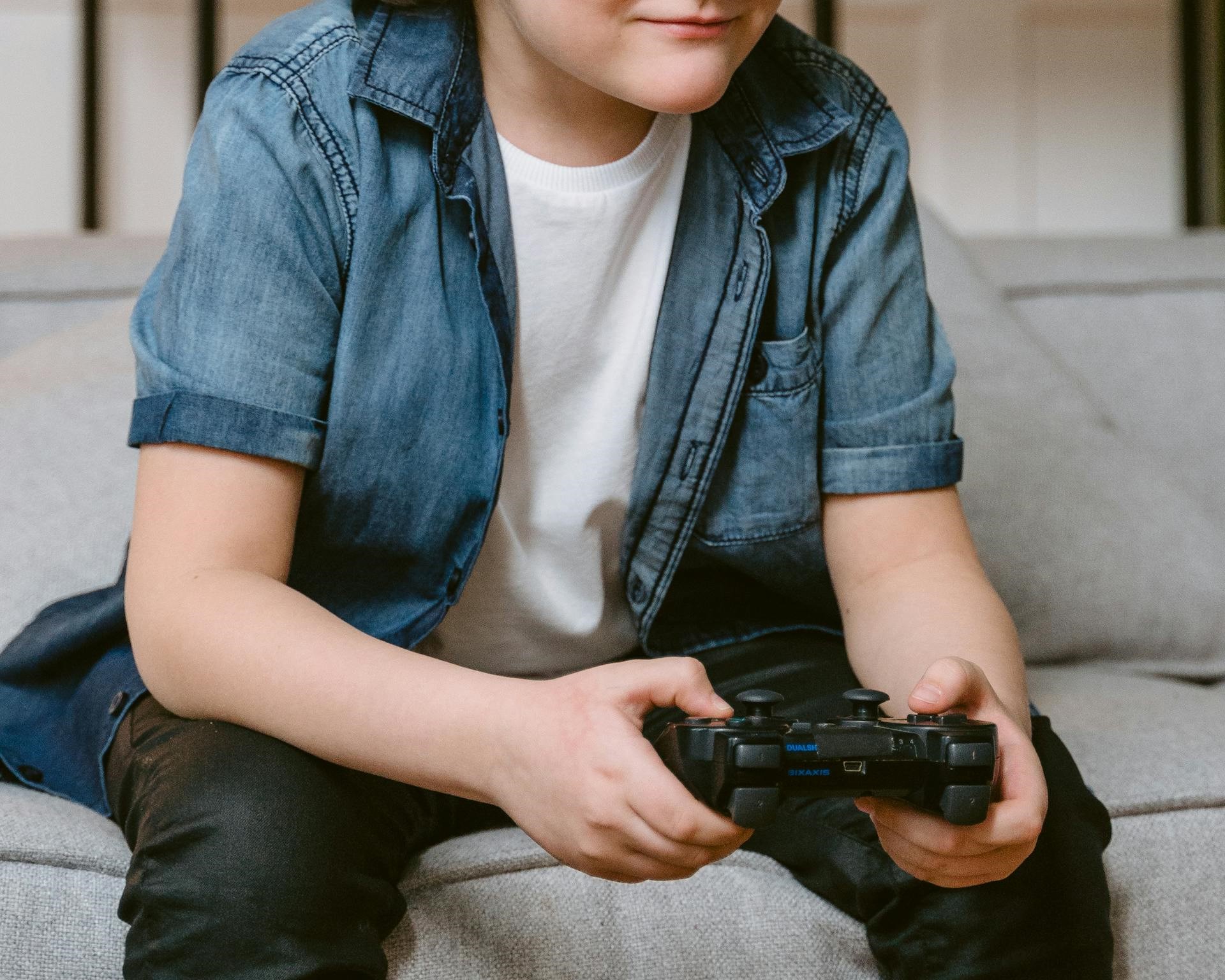 Un garçon assis sur le canapé et tenant une manette de jeu | Source : Pexels